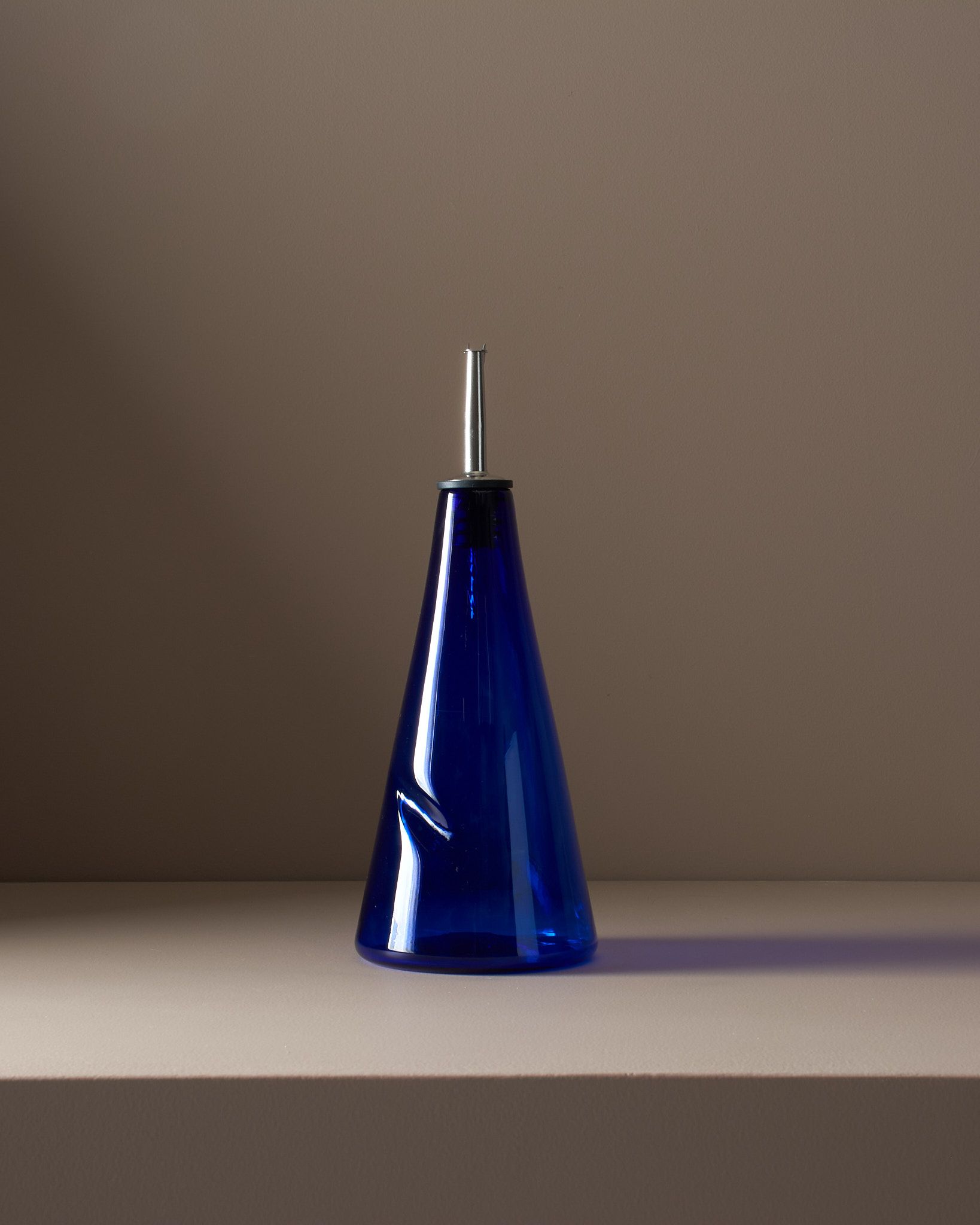 A studio photo of pair of handblown blue glass pour bottle on a brown plinth