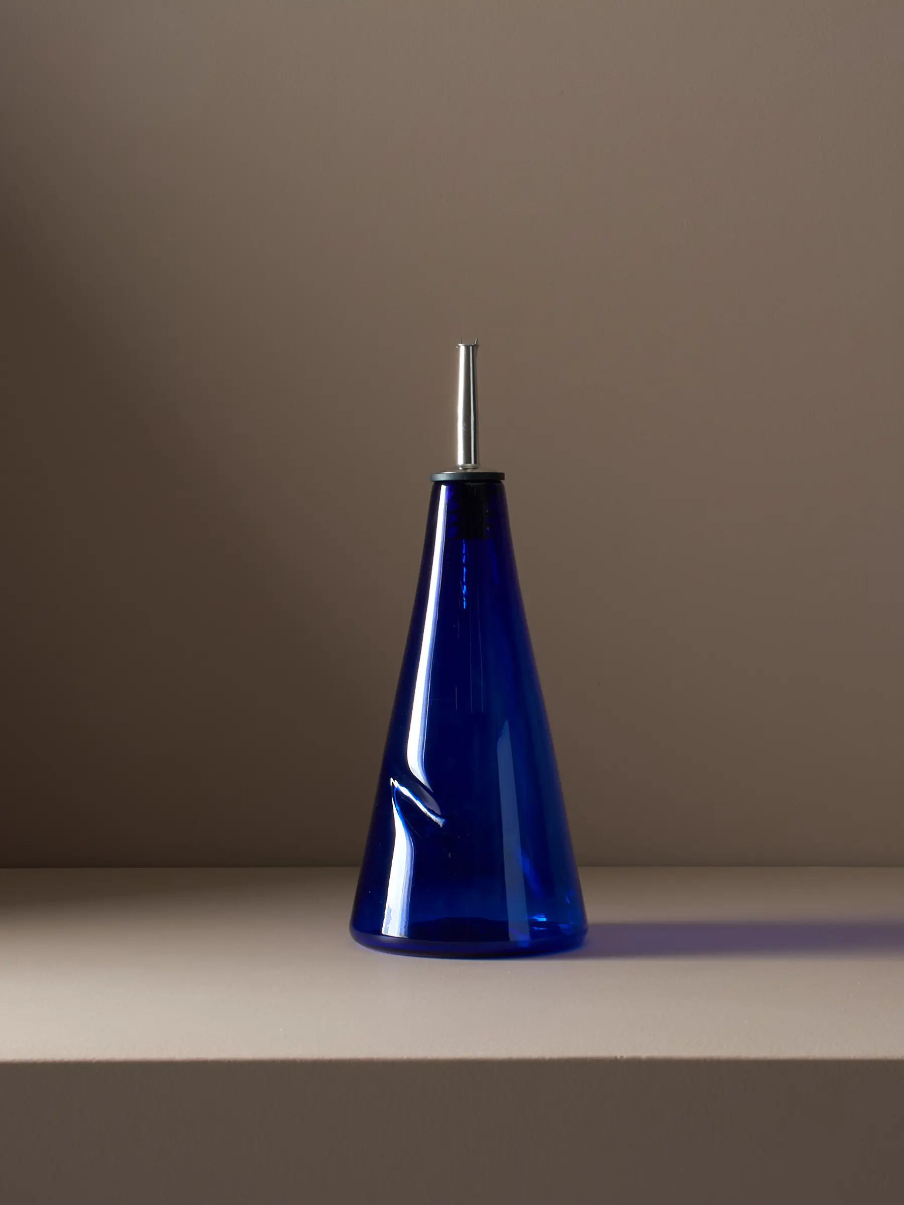 A studio photo of pair of handblown blue glass pour bottle on a brown plinth