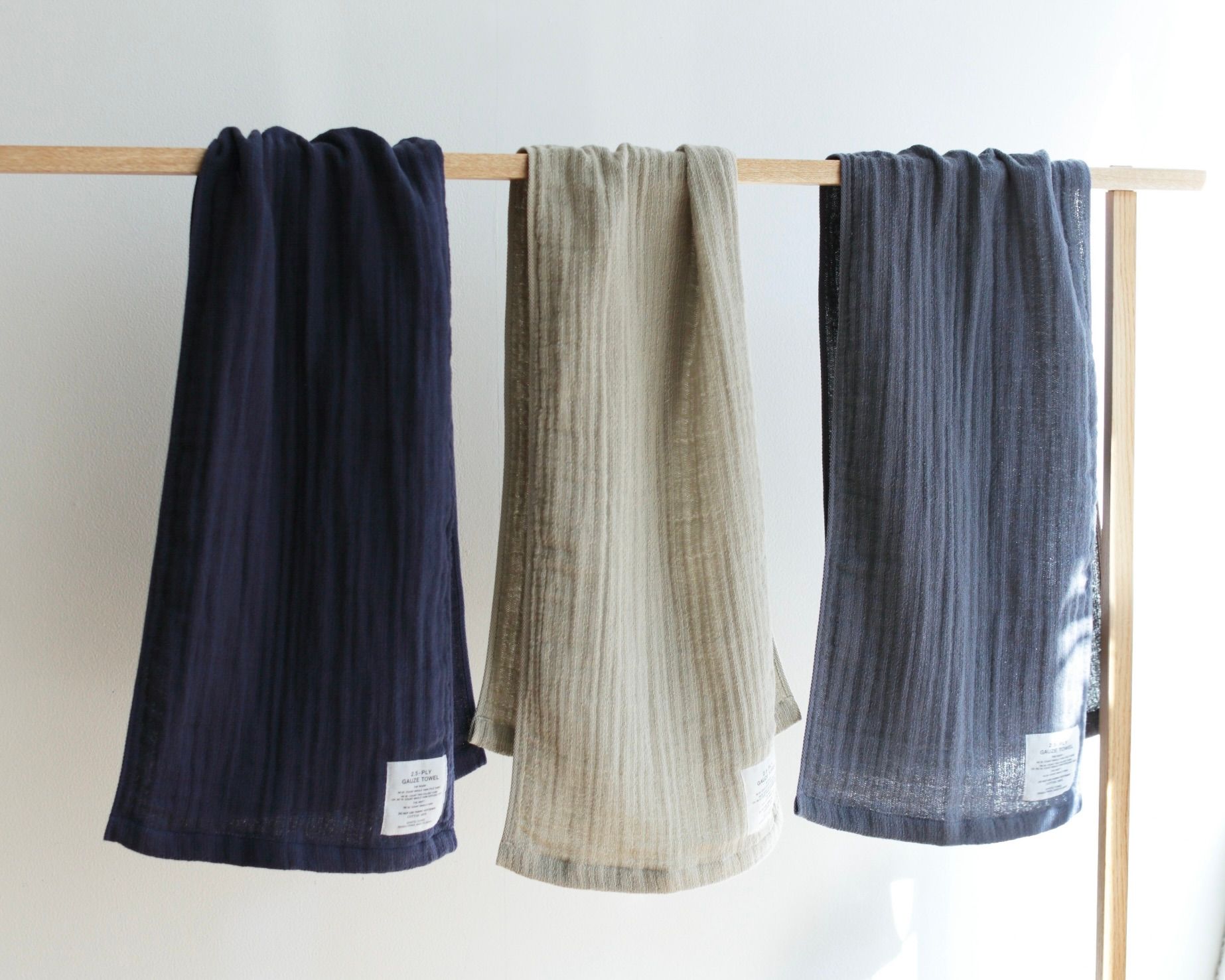 A collection of three Shinto Gauze Hand towels hanging on a wooden rail with a white background 