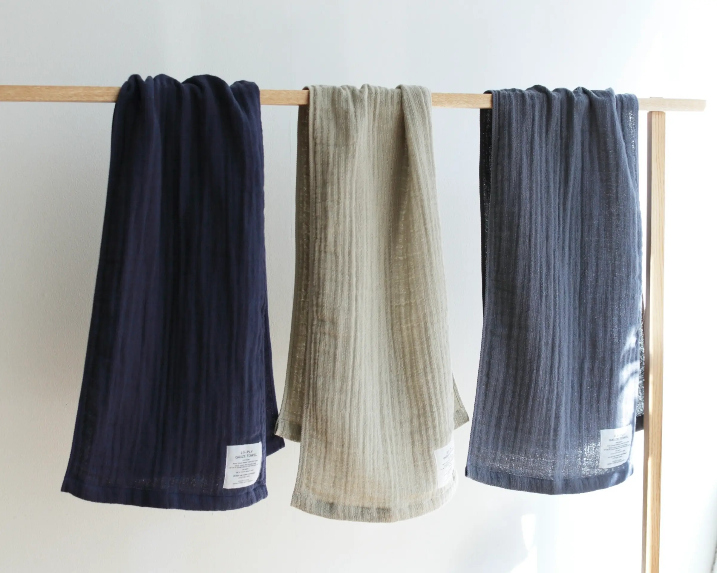 A collection of three Shinto Gauze Hand towels hanging on a wooden rail with a white background