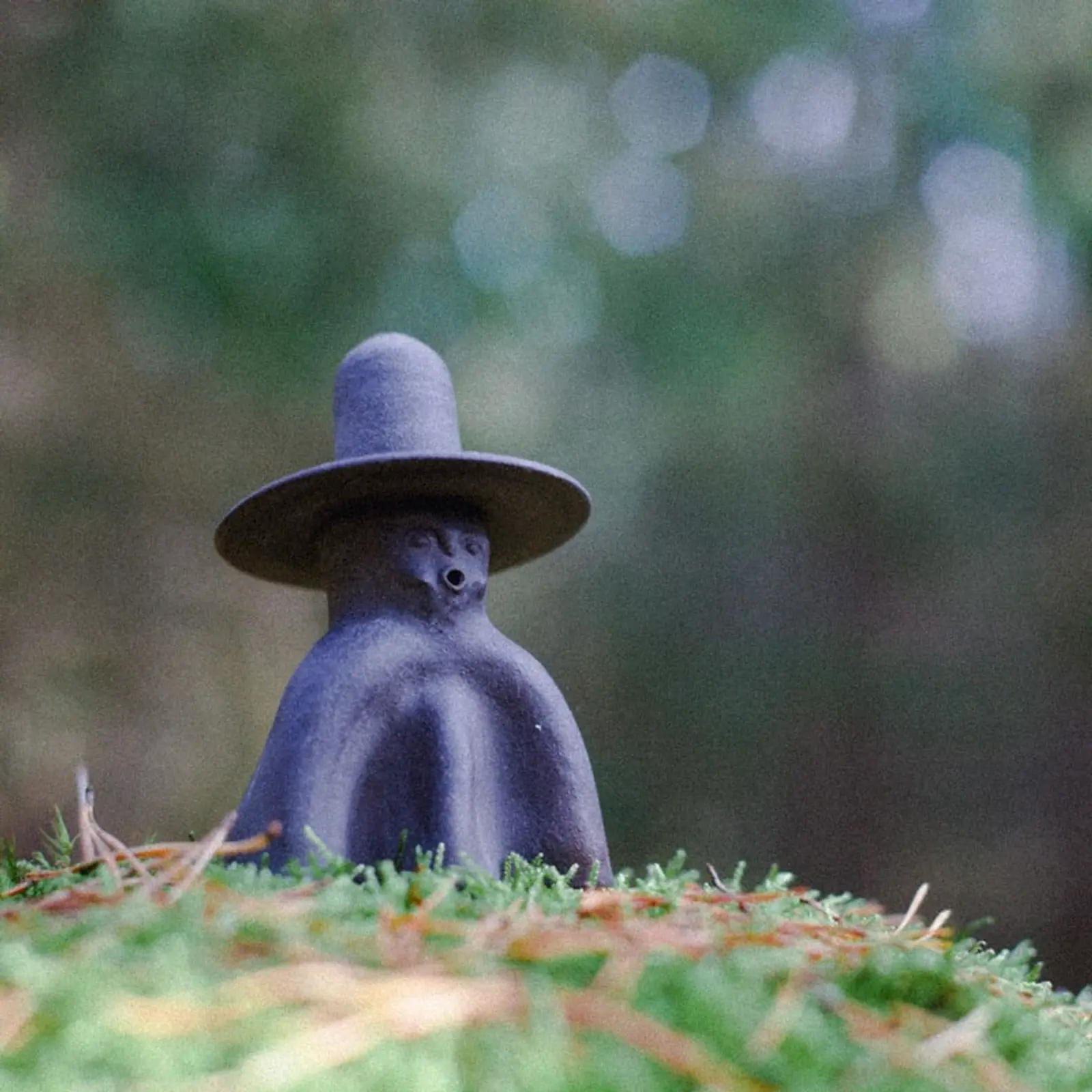 a ceramic incense burner figure with a face and tall wide brim hat on a grassy bed
