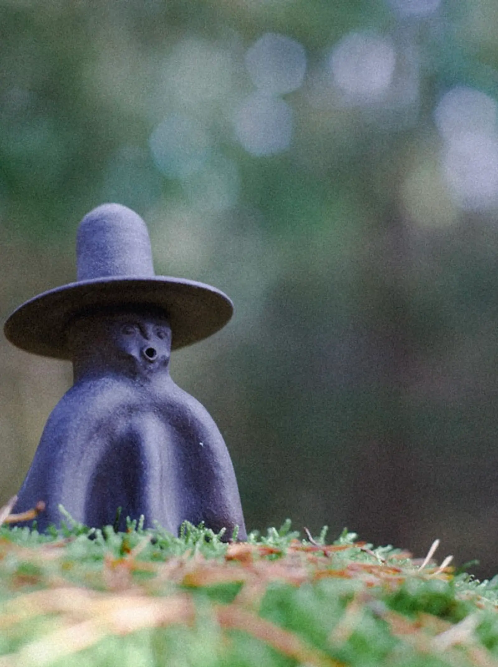 a ceramic incense burner figure with a face and tall wide brim hat on a grassy bed