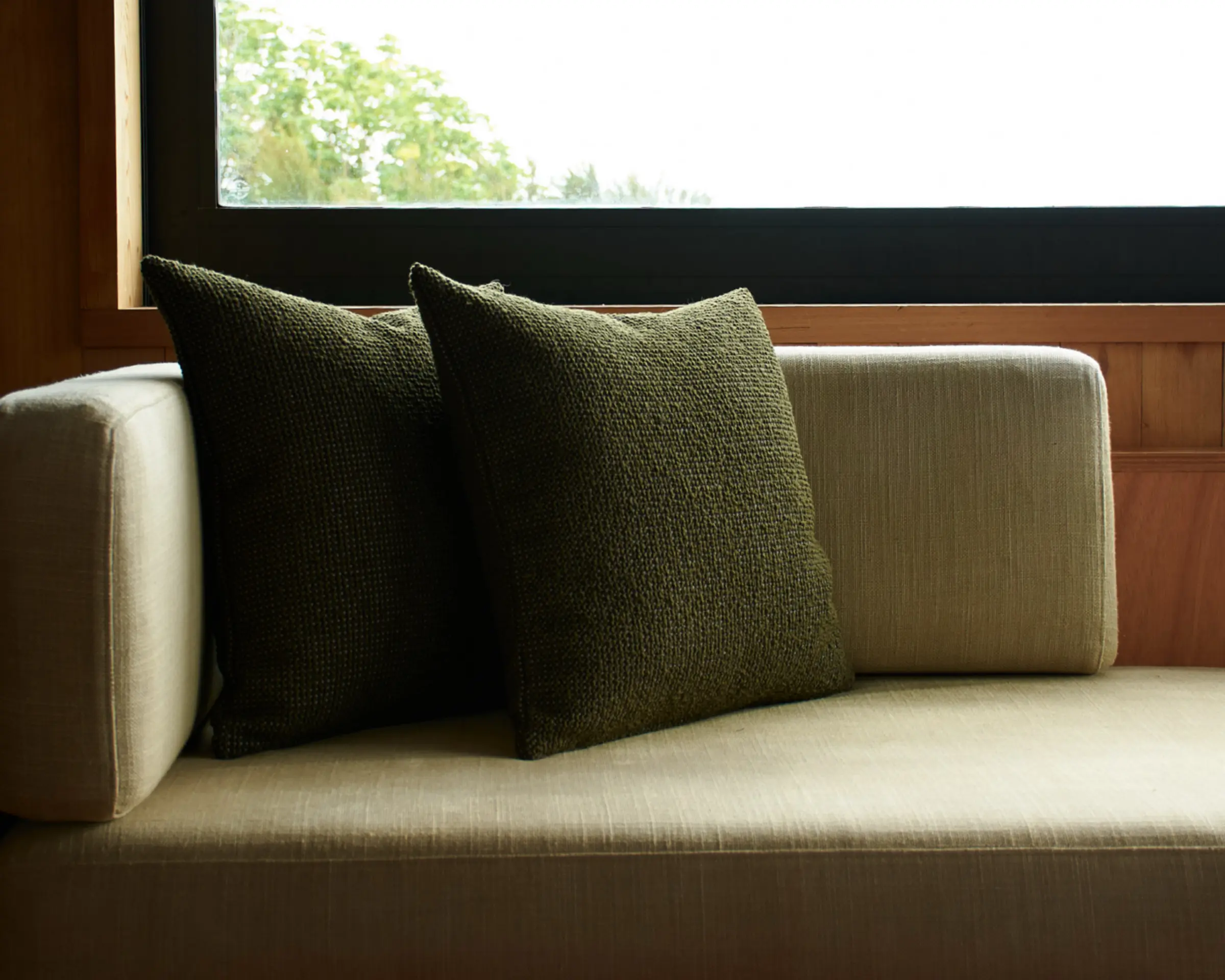 olive green wool cushions on an inset couch next to a window