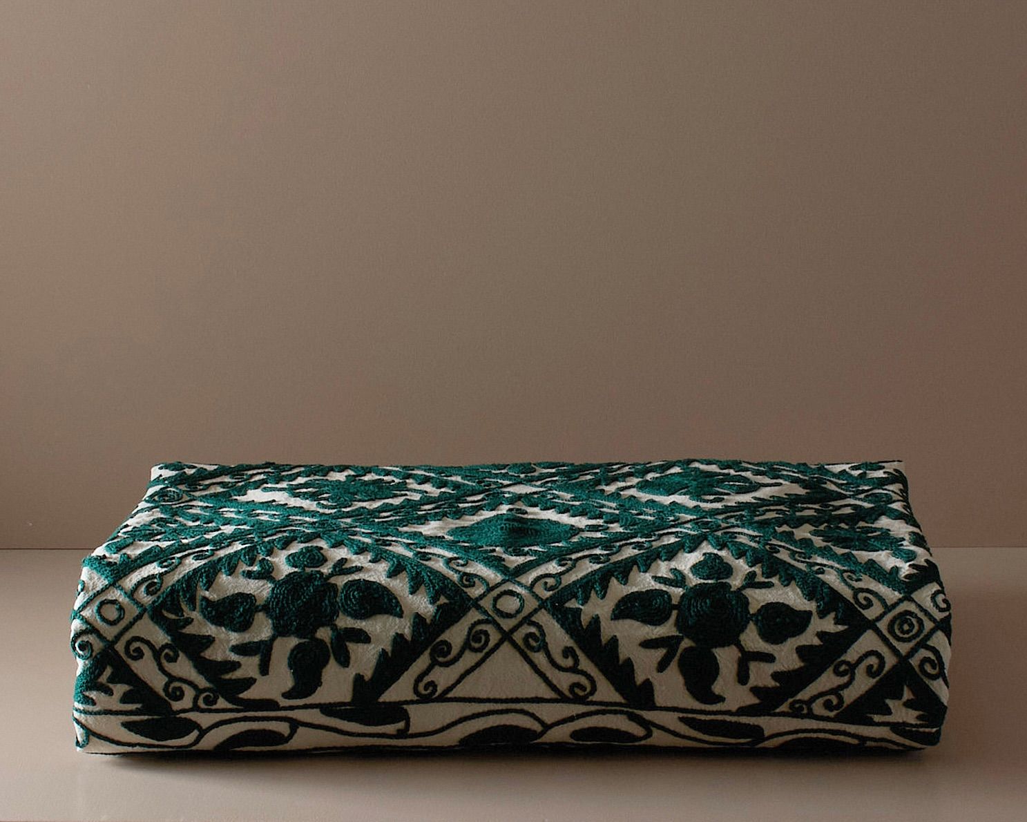 An embroidered suzani bedcover on a neutral colored plinth 