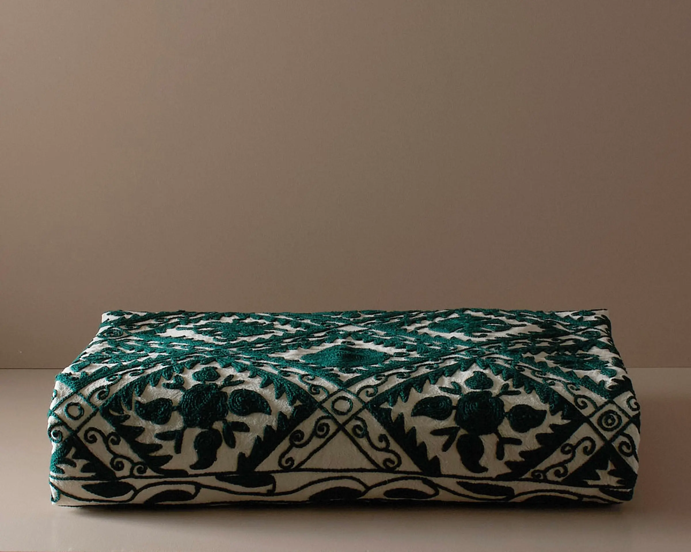 An embroidered suzani bedcover on a neutral colored plinth