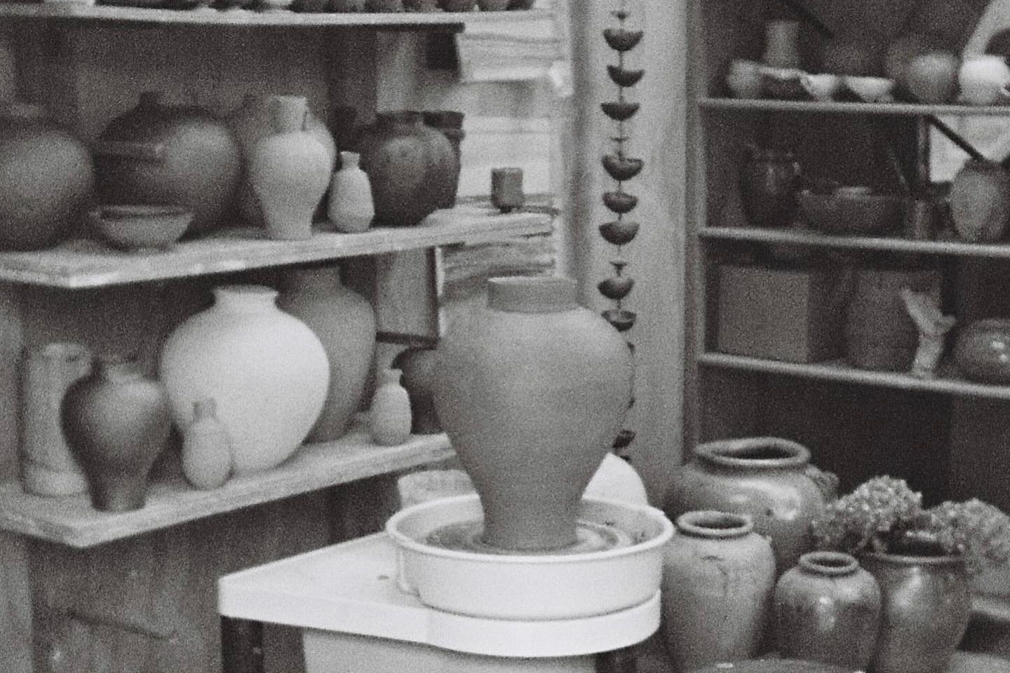 a collection of Pottery from Holly Rose Morgan with shelves covered in ceramic vases and a moon shaped vase sitting on the pottery wheel