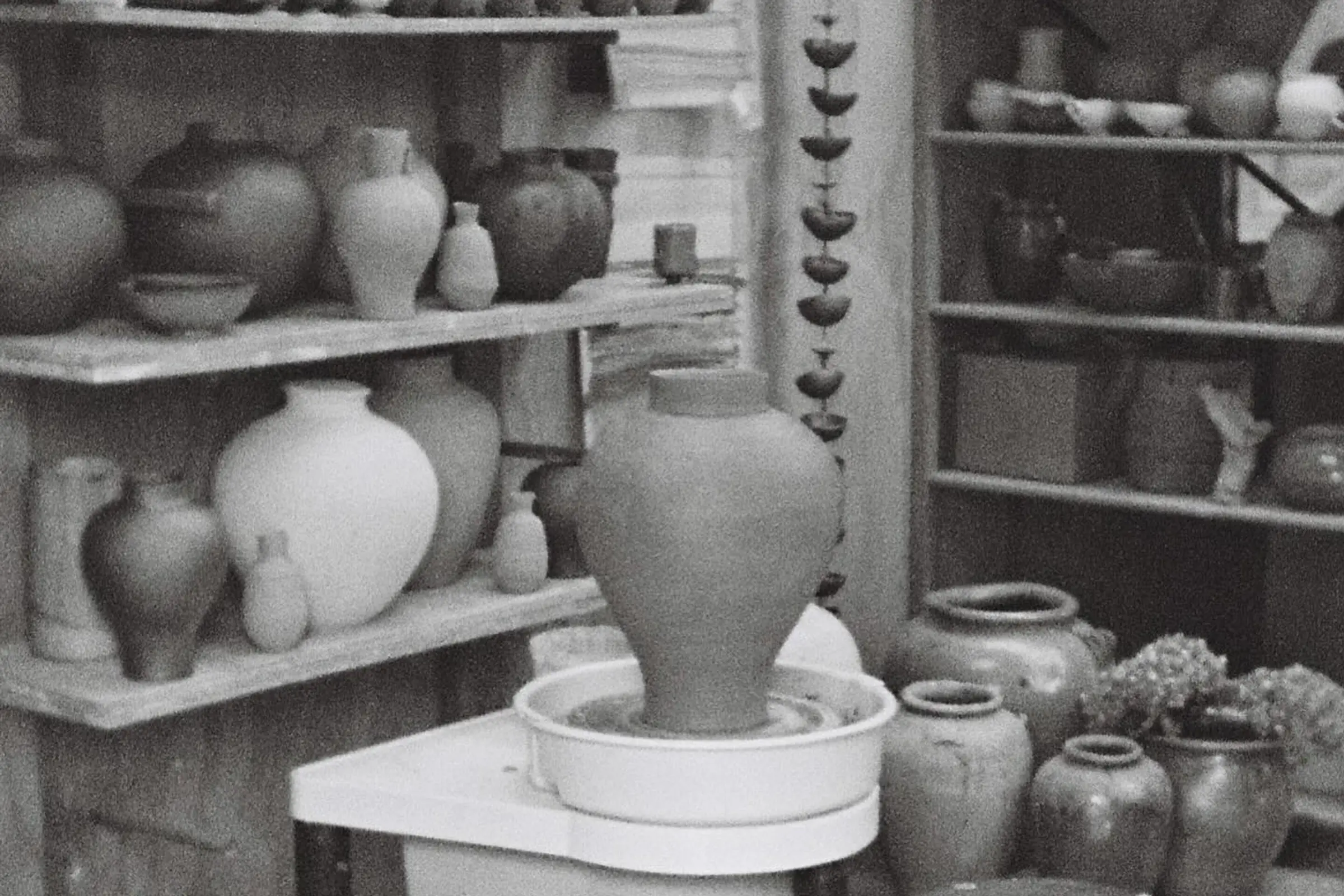a collection of Pottery from Holly Rose Morgan with shelves covered in ceramic vases and a moon shaped vase sitting on the pottery wheel