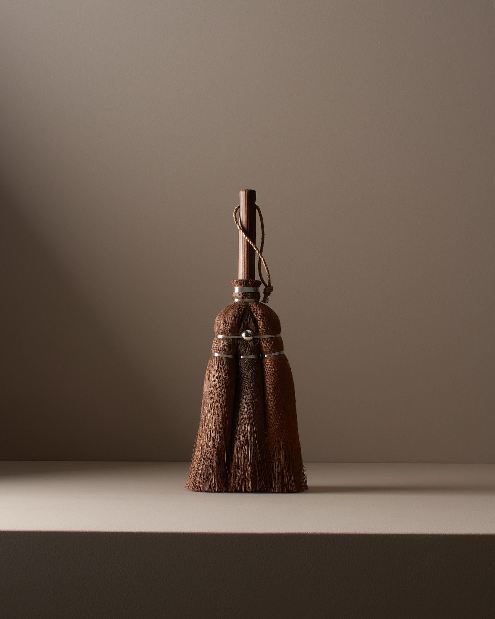 A handmade Japanese Cypress hand broom studio shot standing on a brown plinth with moody single lighting from one side