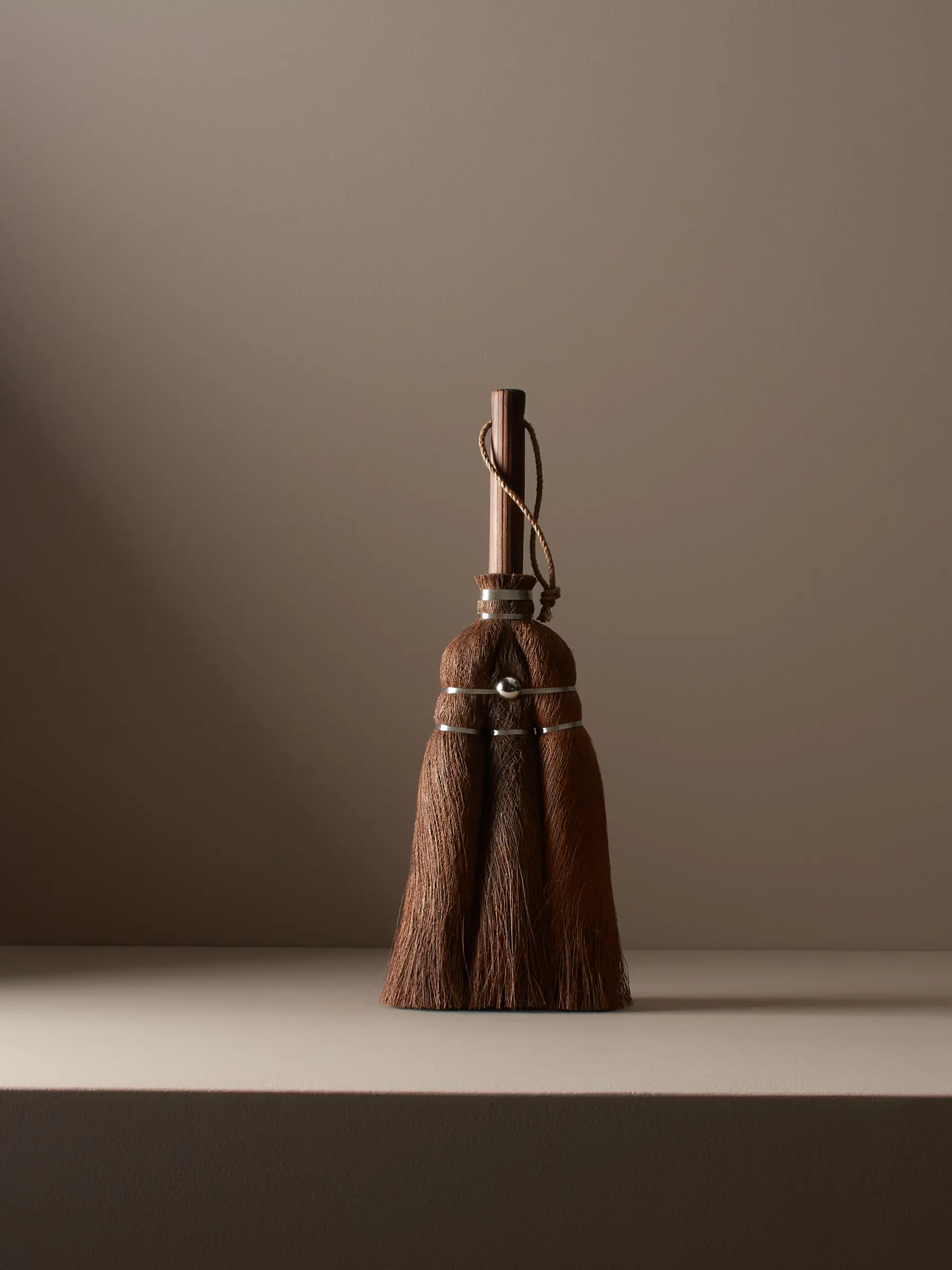 A handmade Japanese Cypress hand broom studio shot standing on a brown plinth with moody single lighting from one side