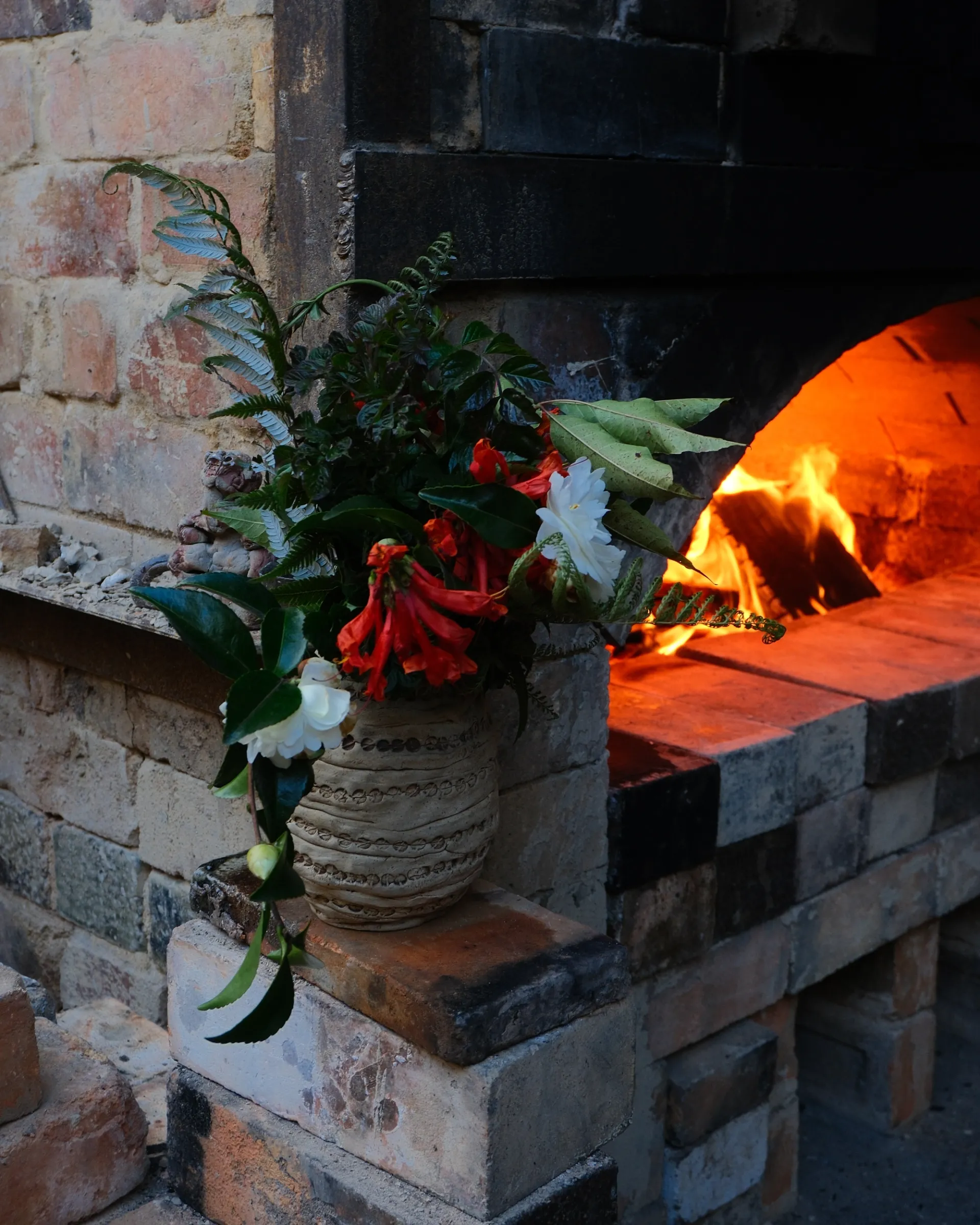 A wood fired kiln made from bricks with a ceramic vase filled wth flowers and a fire burning behind it at Driving creek pottery in the Coromandel of New Zealand