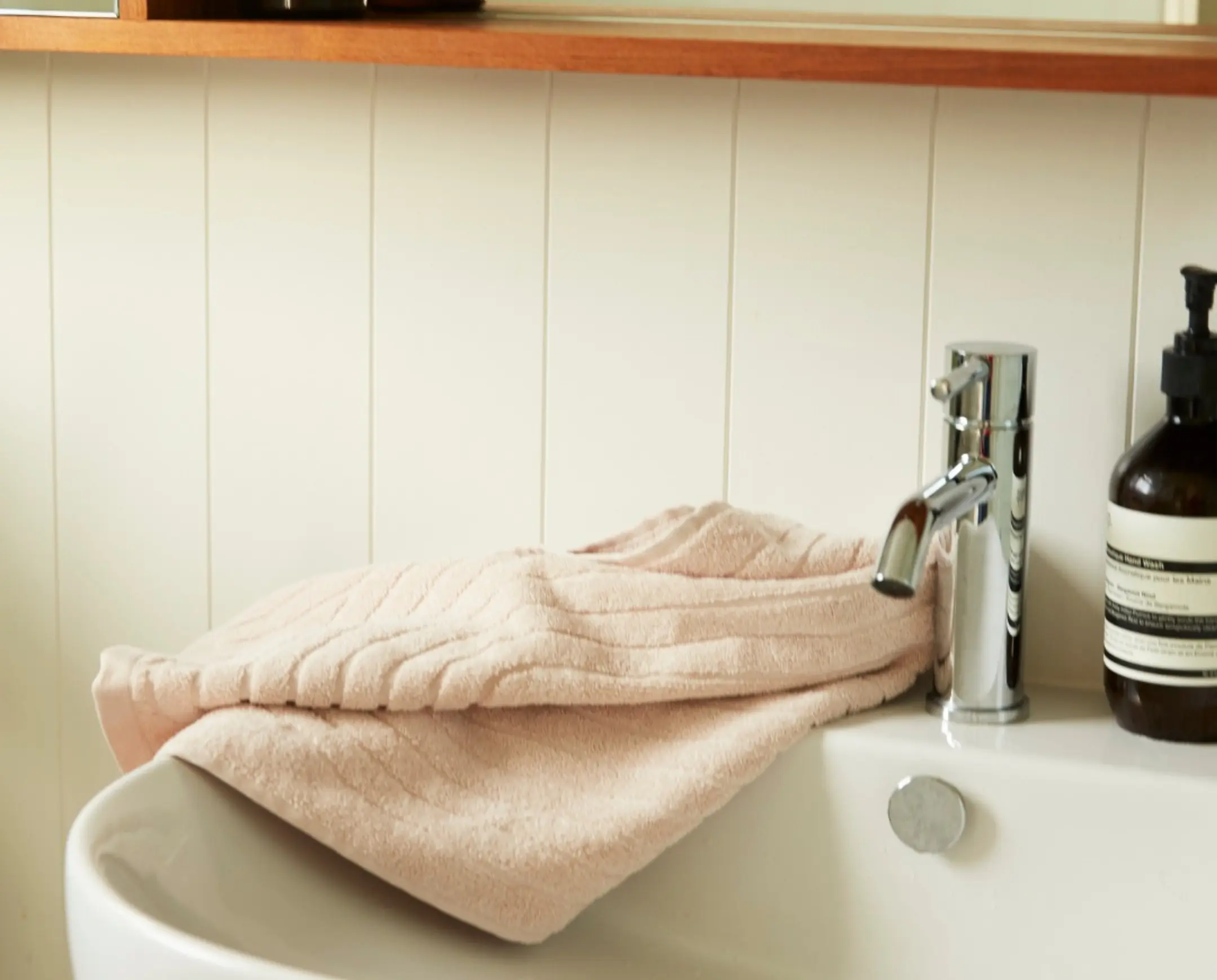 Pale pink hand towel draped over the edge of a white sink with hand soap next to it