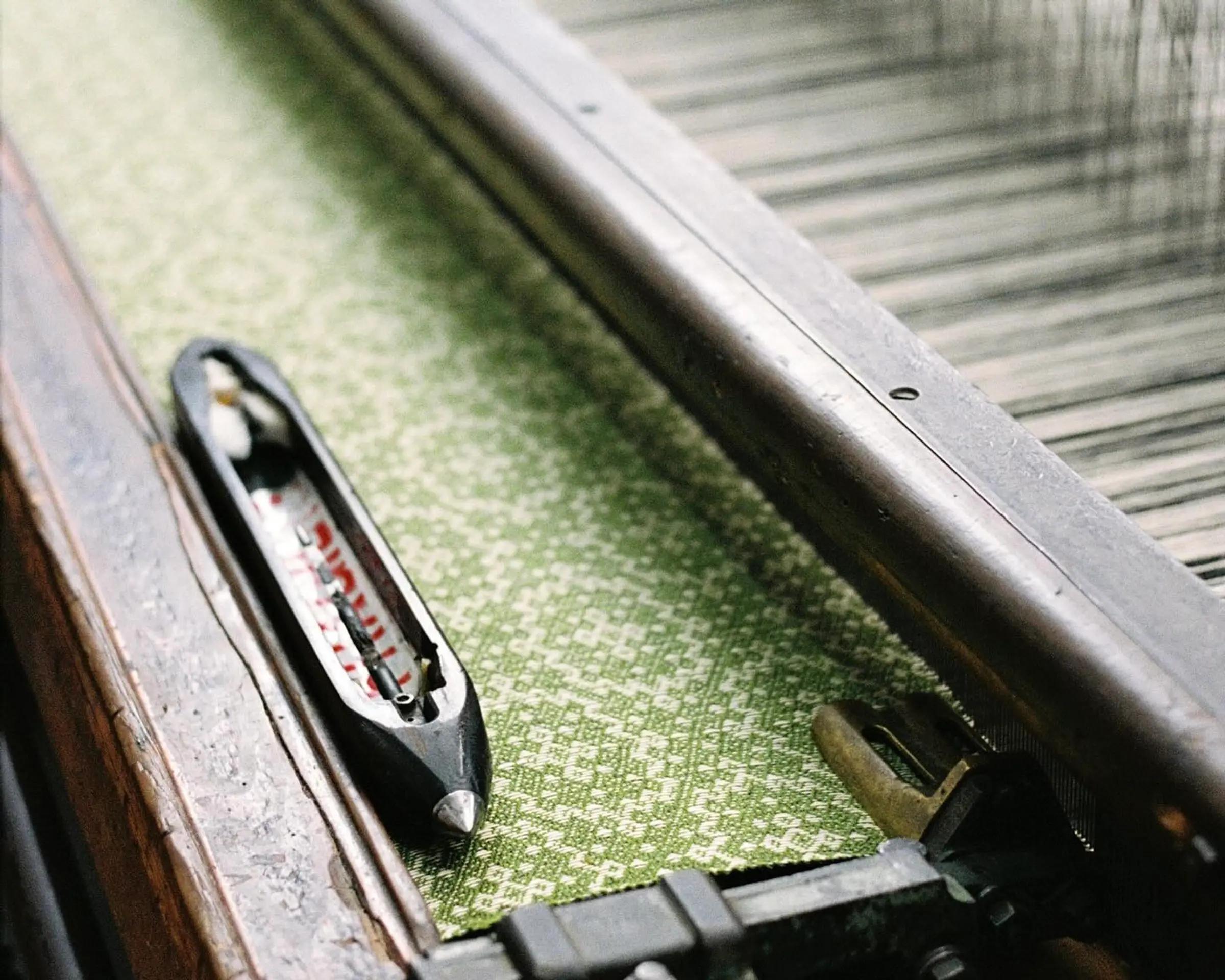 A weaving tool used in blanket and textile making sat ontop of a loom in Burels factory, you can see a green and cream design textiles strung up