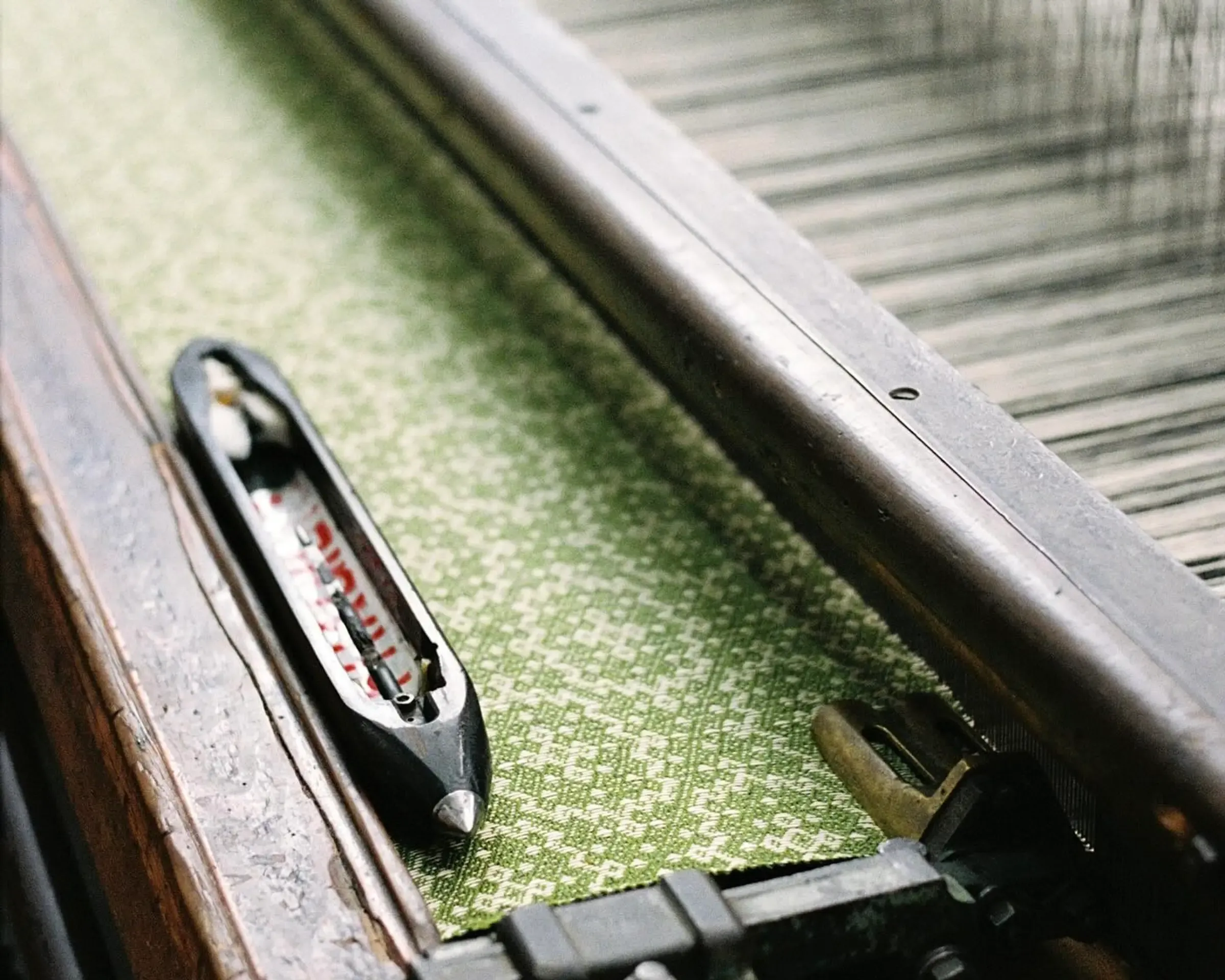 A weaving tool used in blanket and textile making sat ontop of a loom in Burels factory, you can see a green and cream design textiles strung up
