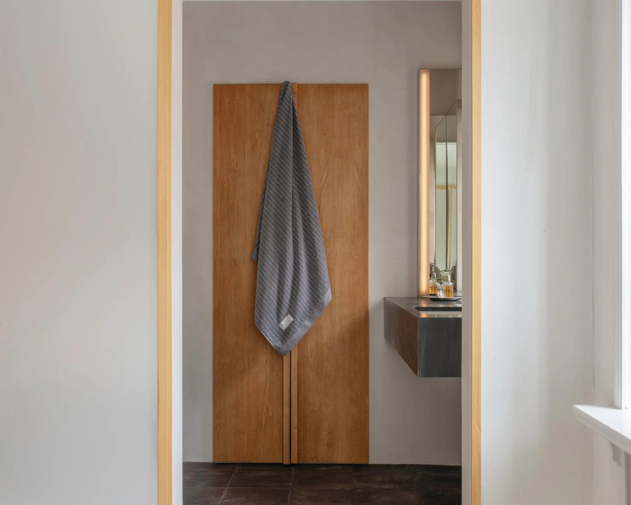 A 100% organic cotton striped bath towel made in Portugal by Magniberg based in Sweden, hanging off a cabinet in a bathroom