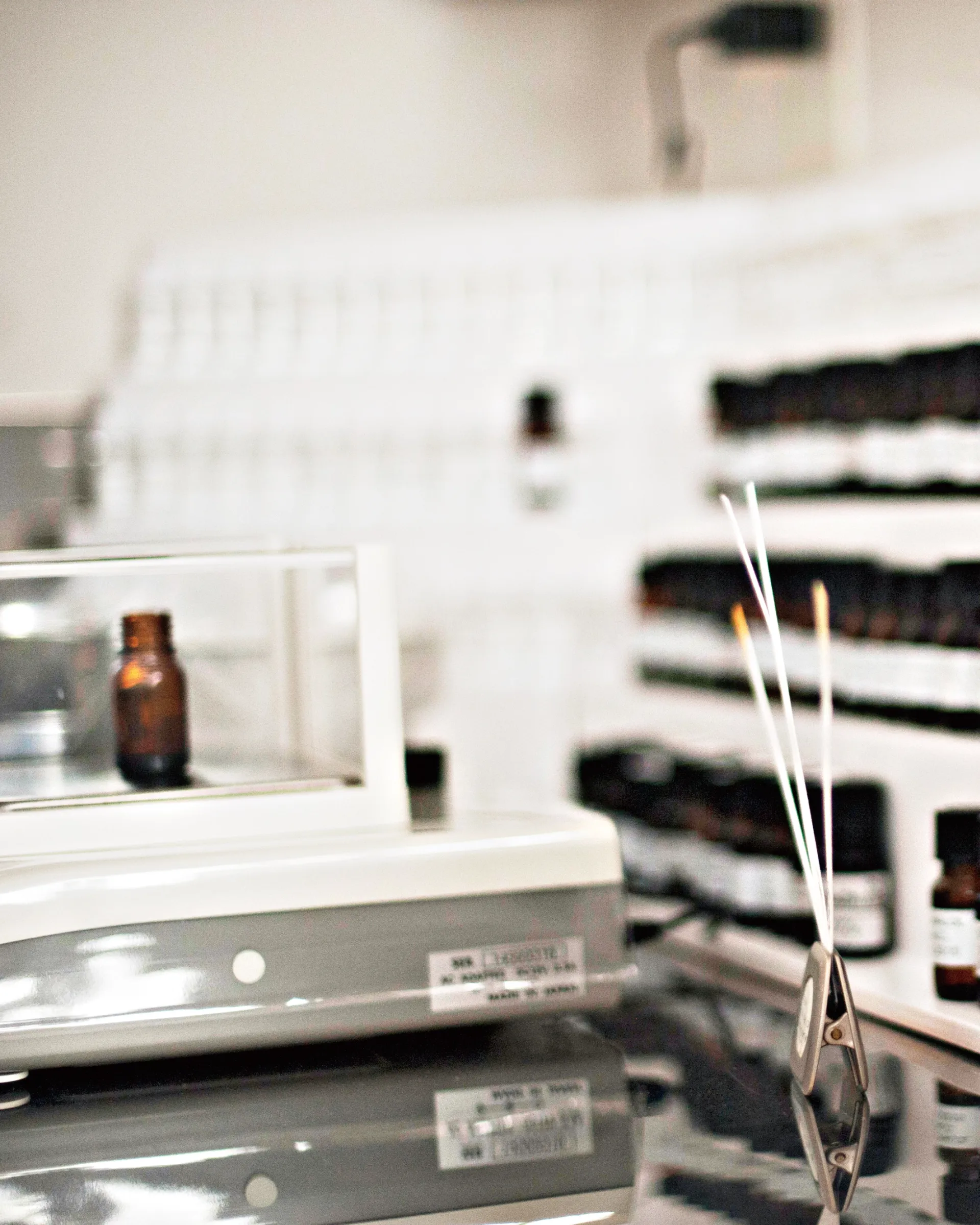 Small sample bottles of fragrance on a small white shelf with test strips infront of them