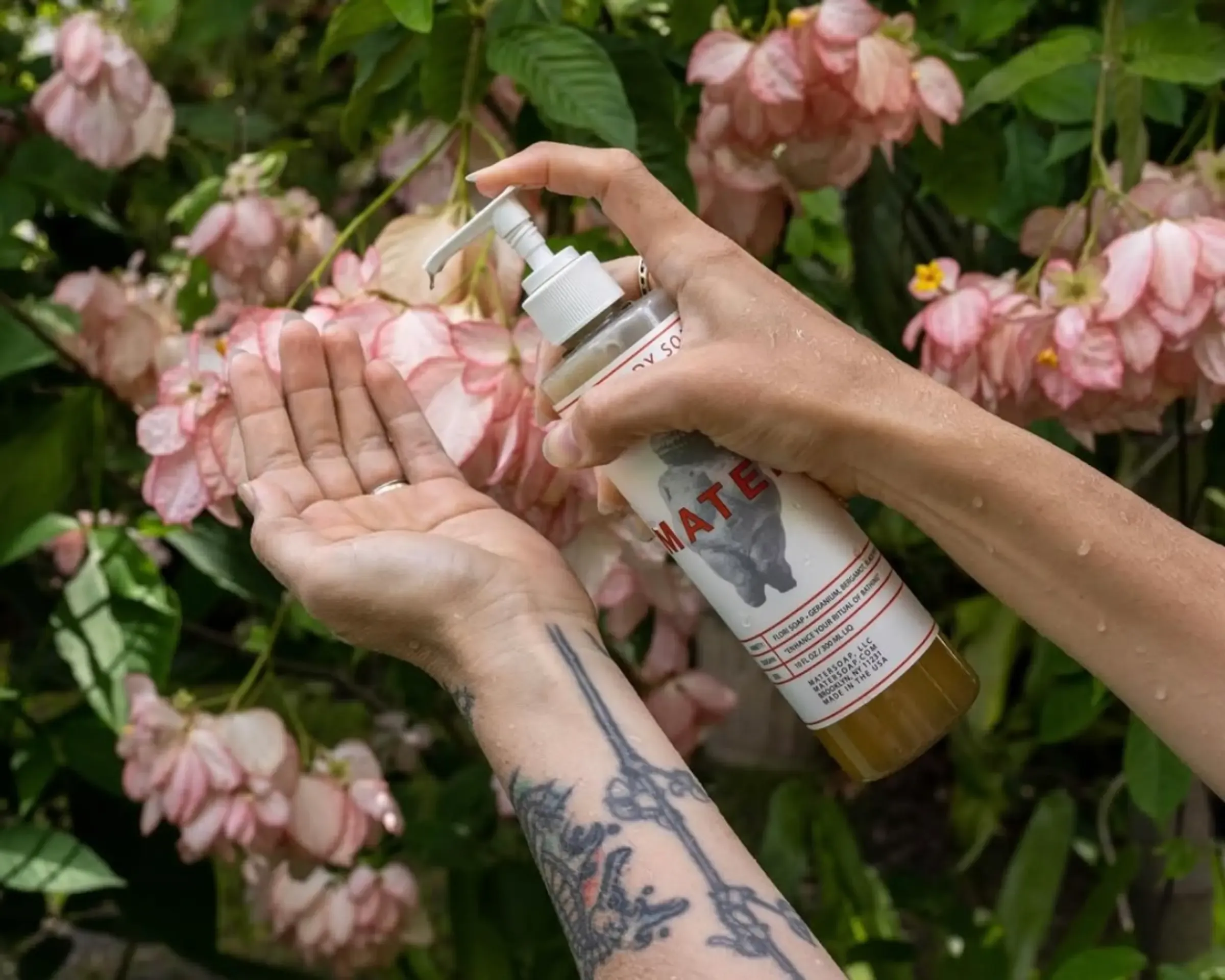mater flori liquid hand soap squeezing onto a hand with a wall of flowers in the background