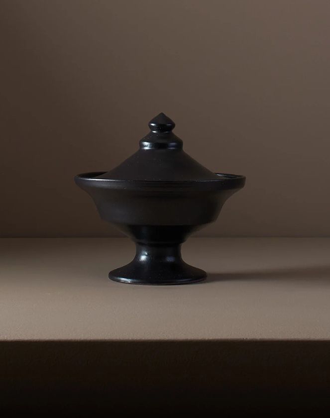 A ceramic Black lidded vessel from Kirsten Druburgh pottery with a pointed lid, shape inspired from Etruscan pottery, sitting on a brown background
