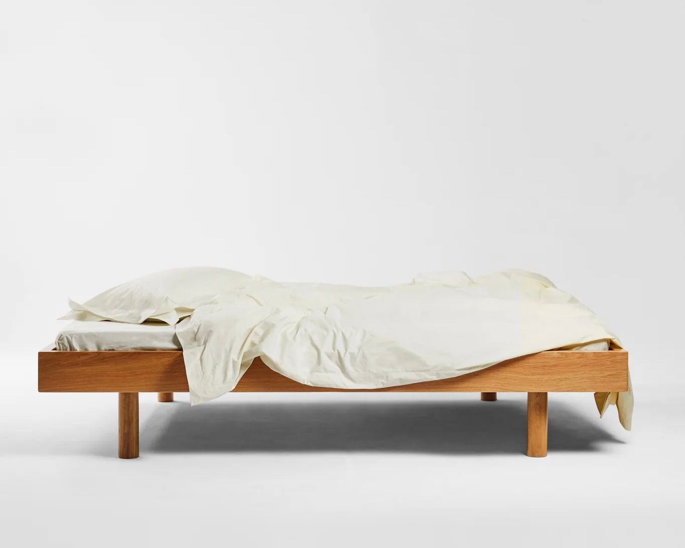 SUTRAM Canvas Organic Cotton Percale Fitted Sheet made in India from 300 thread count organic cotton percale with a fully elasticated 40–45cm depth.Sutrams organic percale cotton bedding on a wooden bed frame with the sheets draped over the edges in the colour Canvas, a soft off white