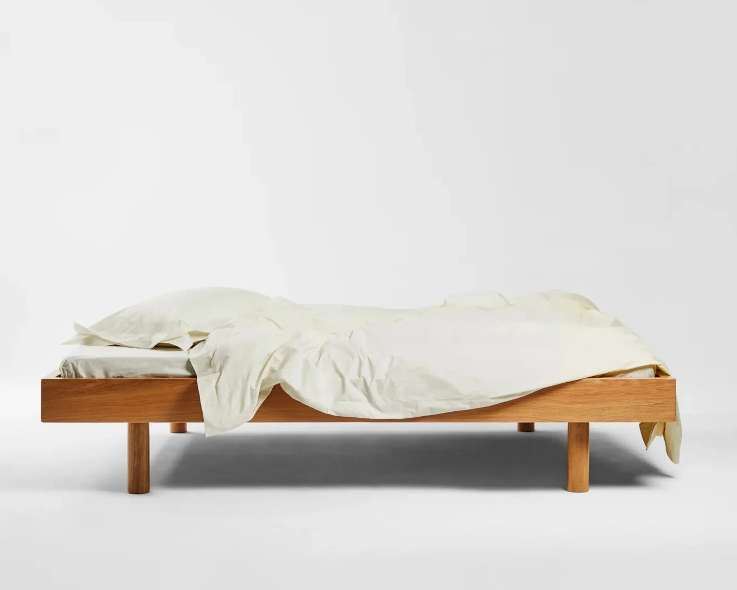 SUTRAM Canvas Organic Cotton Percale Fitted Sheet made in India from 300 thread count organic cotton percale with a fully elasticated 40–45cm depth.Sutrams organic percale cotton bedding on a wooden bed frame with the sheets draped over the edges in the colour Canvas, a soft off white
