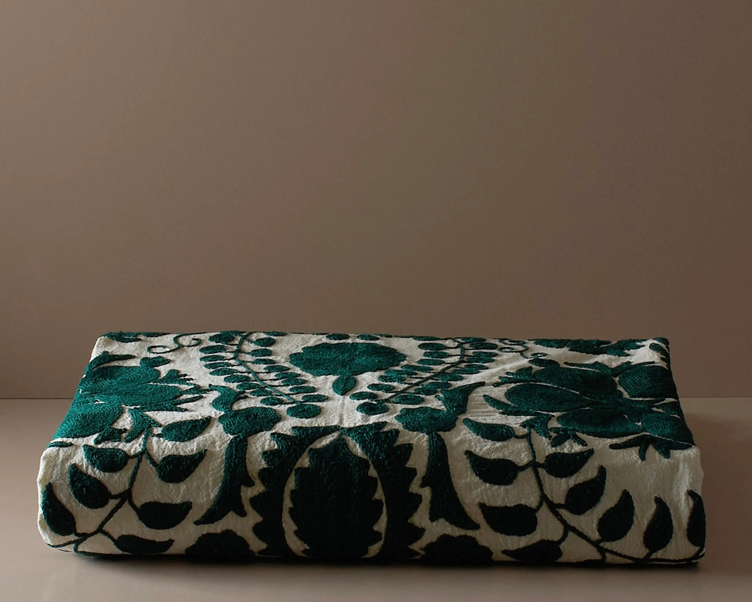 An embroidered suzani bedcover on a neutral colored plinth