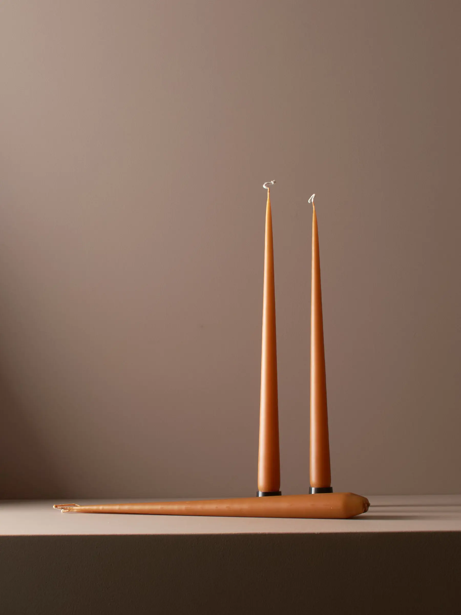 three warm amber taper candles, a studio shot with a warm brown background