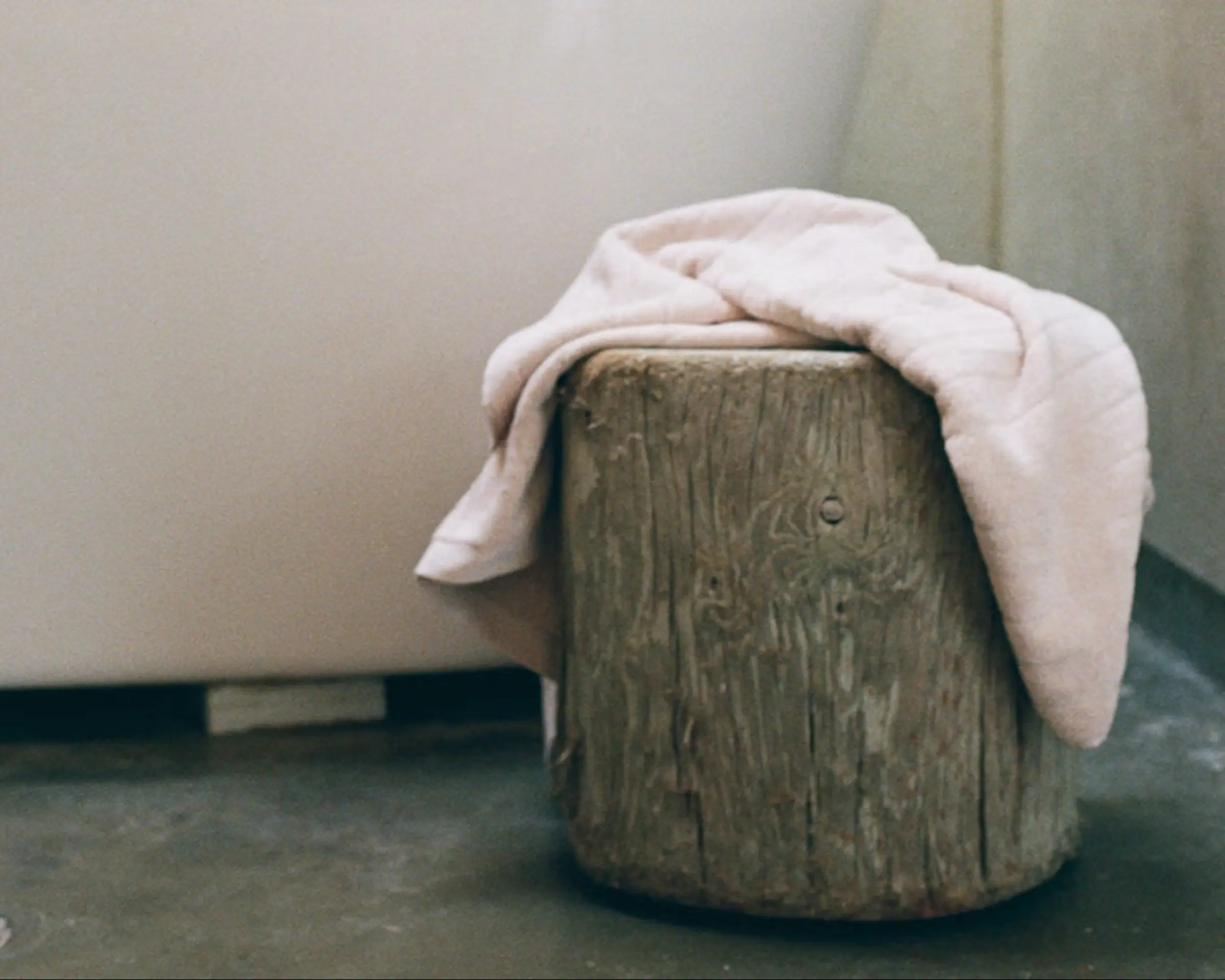 Pale pink bath towel draped over a wooden log next to a bath tub