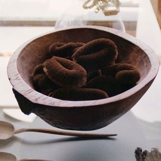 Hand-carved wooden bowl holding dark coiled palm fibre brushes on a windowsill