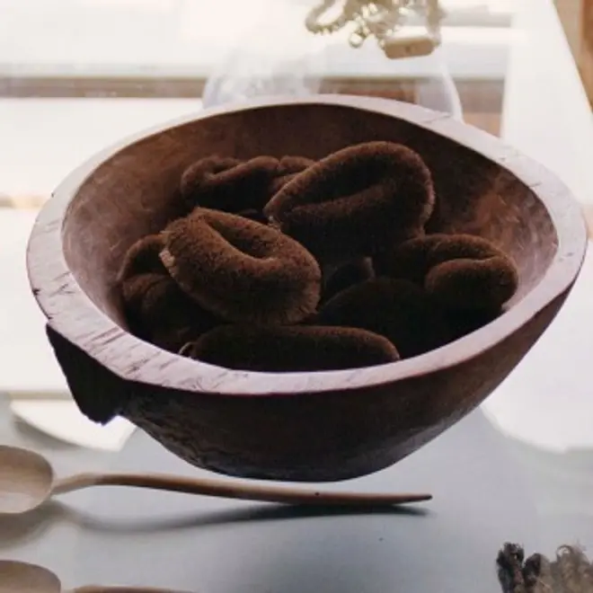 Hand-carved wooden bowl holding dark coiled palm fibre brushes on a windowsill
