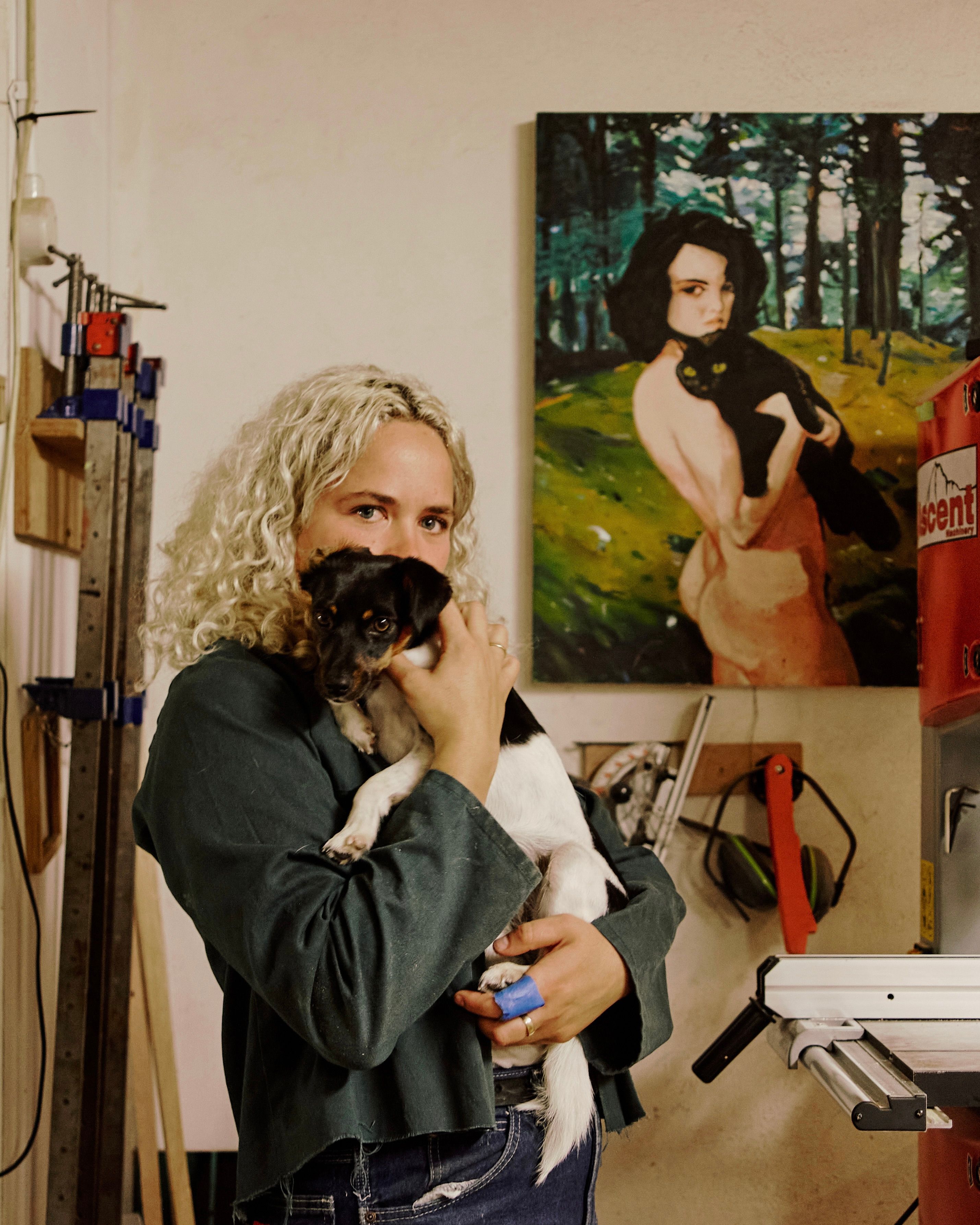 A portrait image of Josephine Jelicich in her wood workshop holding her dog