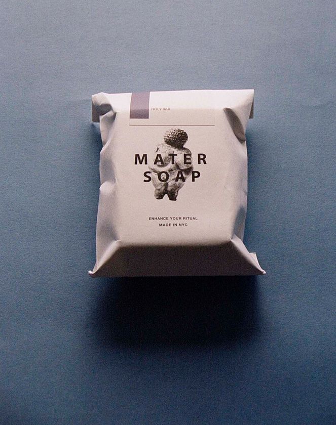 An image of Mater soaps Holy bar of soap in its paper packaging on a blue background. Cold pressed soap with lavender and patchouli