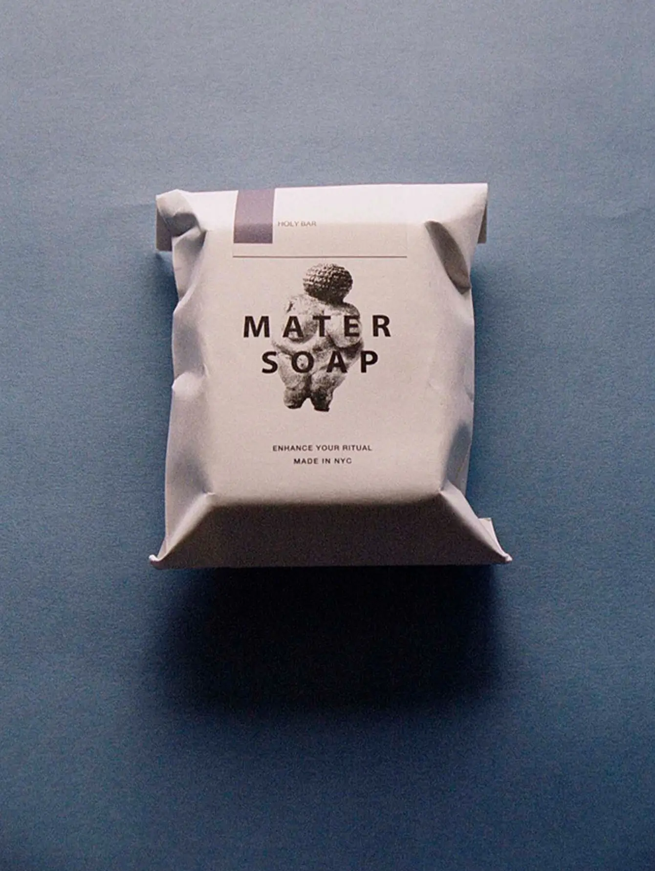 An image of Mater soaps Holy bar of soap in its paper packaging on a blue background. Cold pressed soap with lavender and patchouli