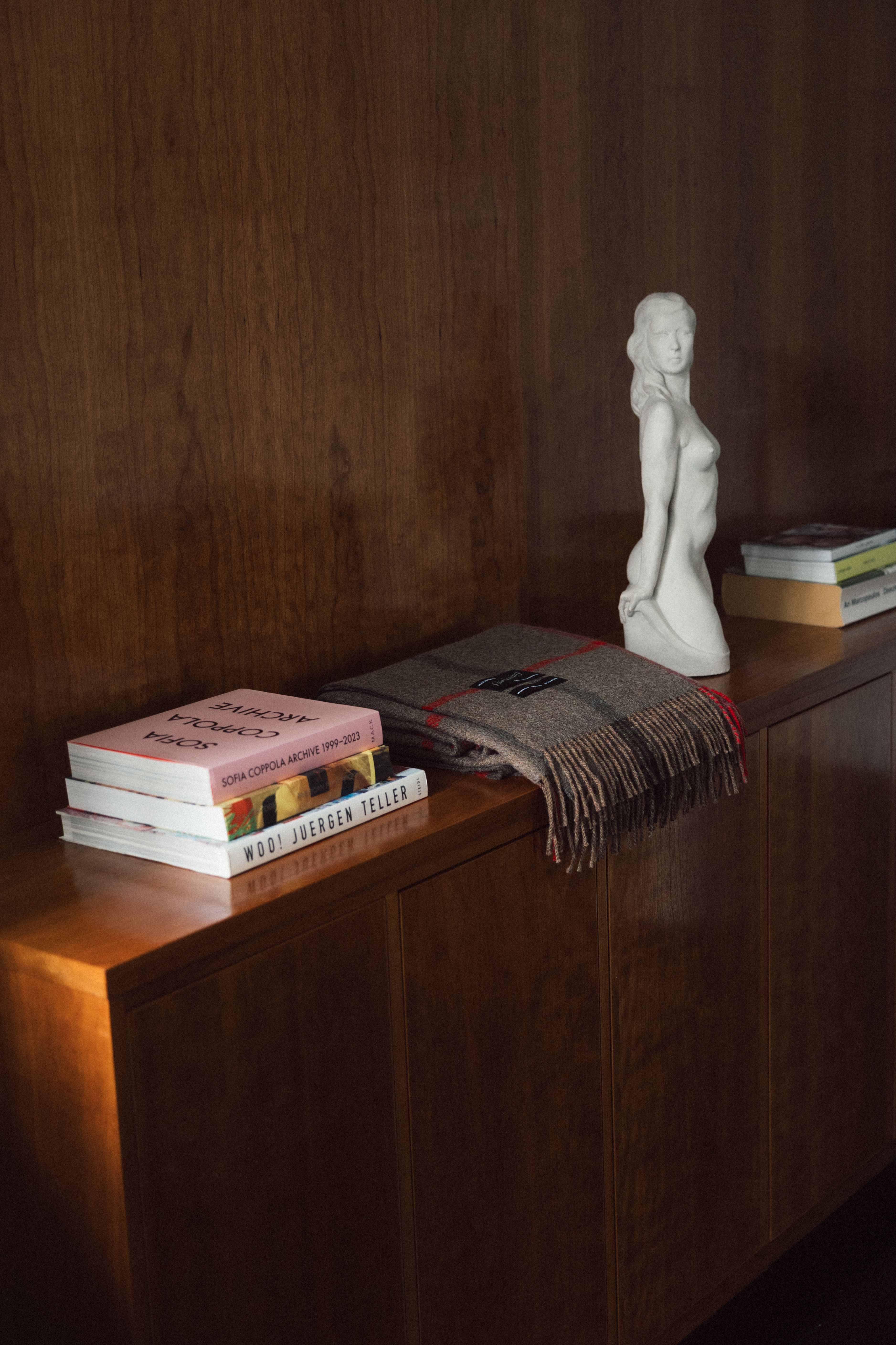 A shot of a magniberg scarf on a side table with books and a sculpture of a woman