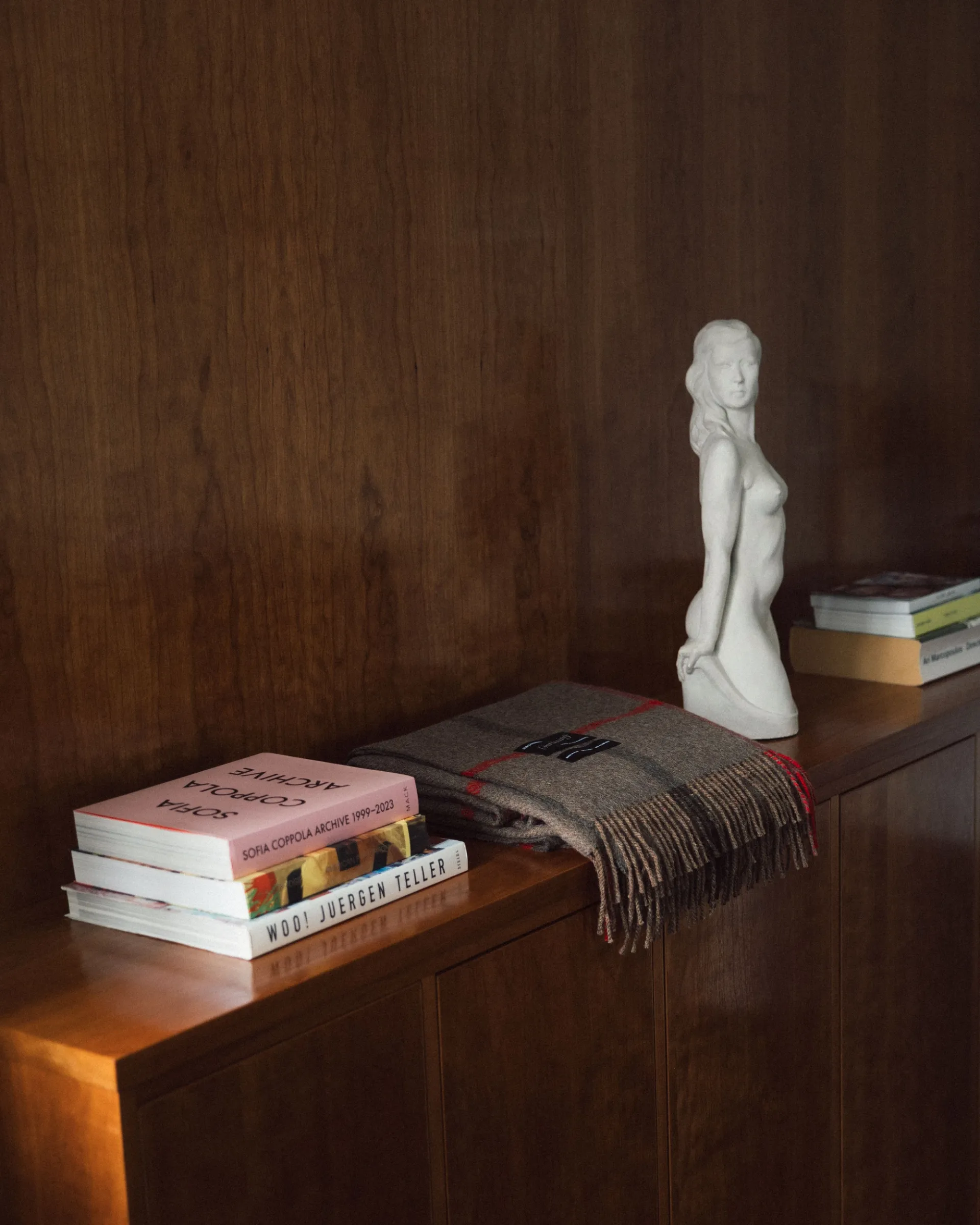 A shot of a magniberg scarf on a side table with books and a sculpture of a woman