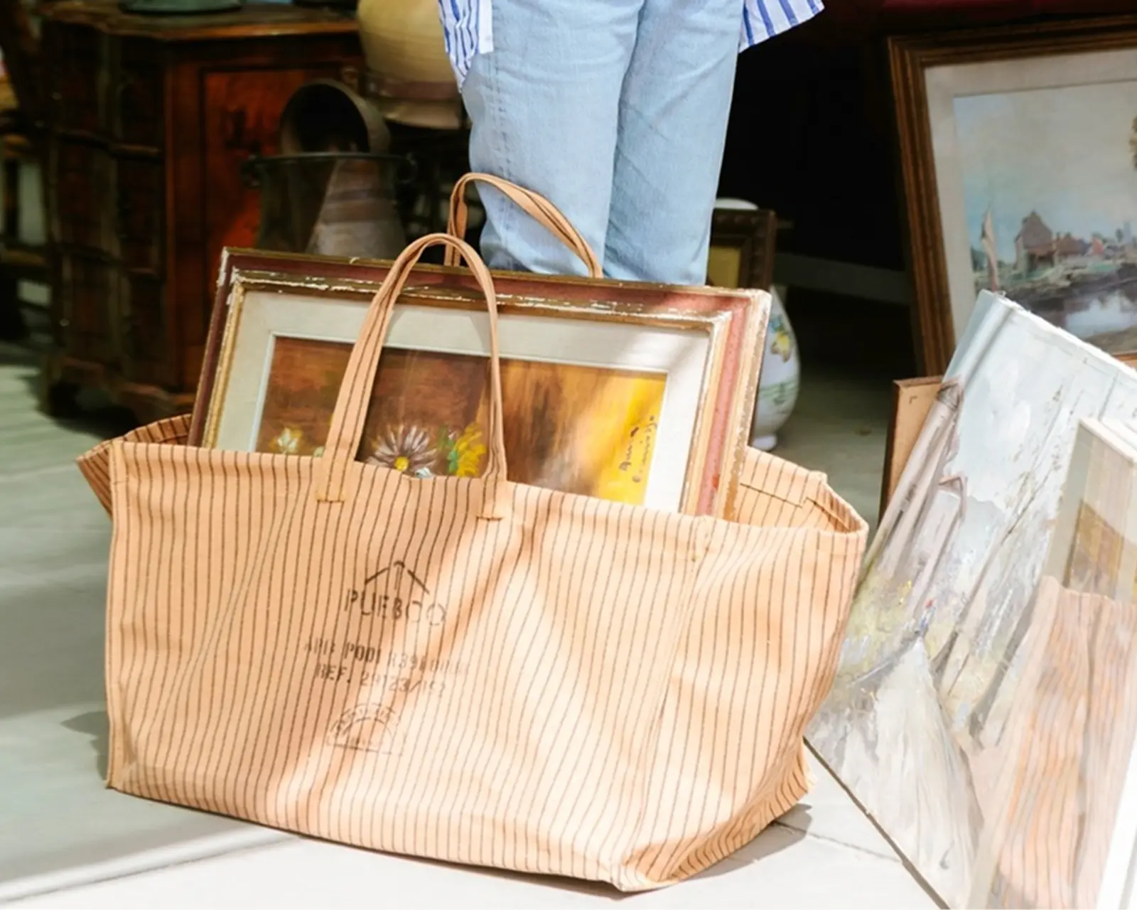 Puebco Waxed Canvas Large Bag in a market setting, carrying framed artwork and vintage finds, crafted from durable waxed cotton with utility-inspired detailing, available at Handcrafted Modern.