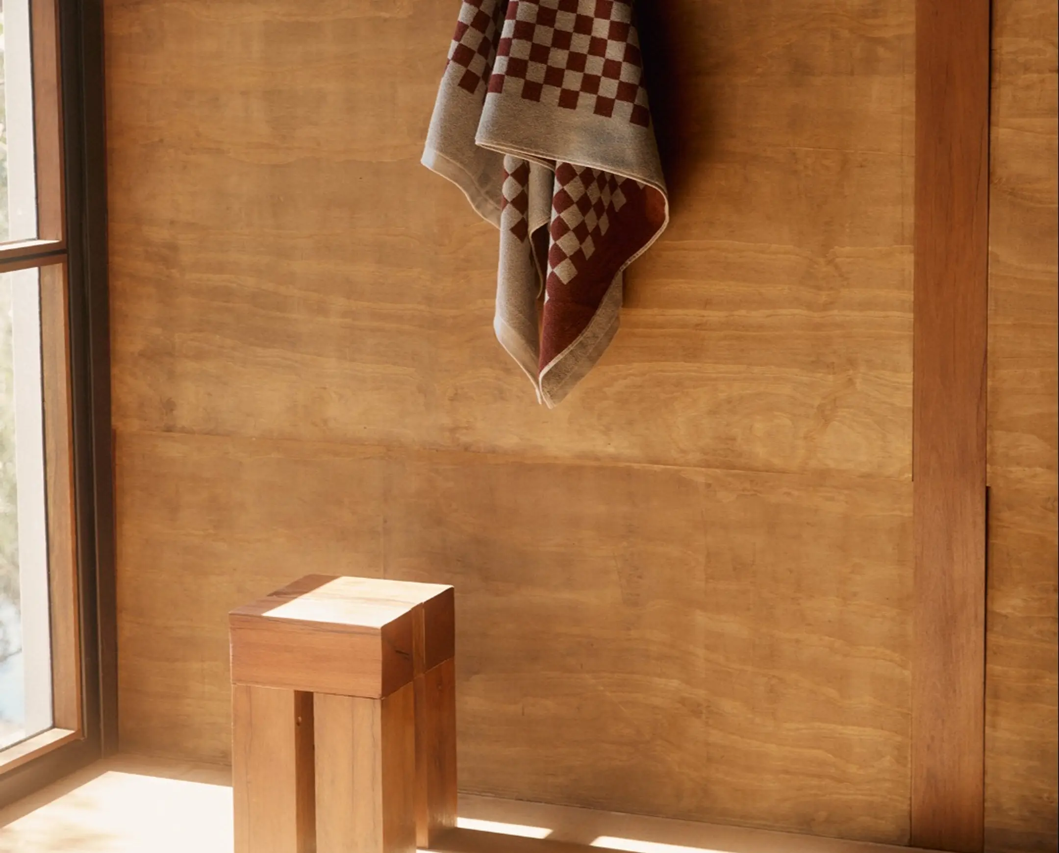 A checkered bath towel hung on a wooden wall with a square wooden stool on the floor