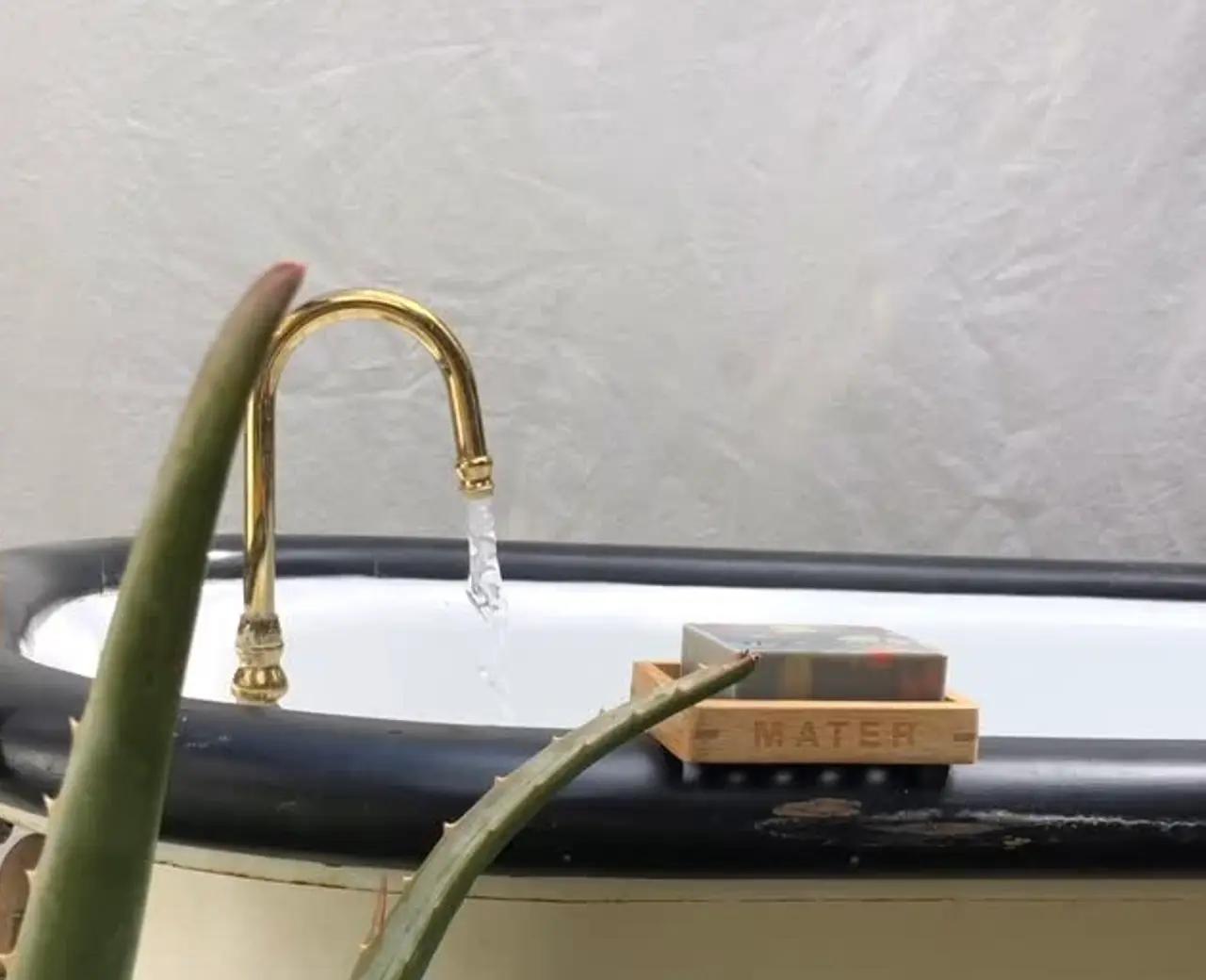 An image from Mater Soap with a bar of their natural cold pressed soap sitting on the side of a bath tub outside with a gold tap