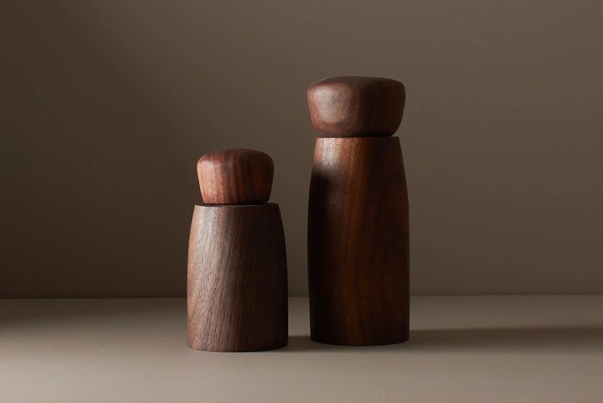 A pair of walnut wood salt and pepper mills in a deep chocolate colour by wood worker Elise McLauchlan from Canada sitting on a brown background