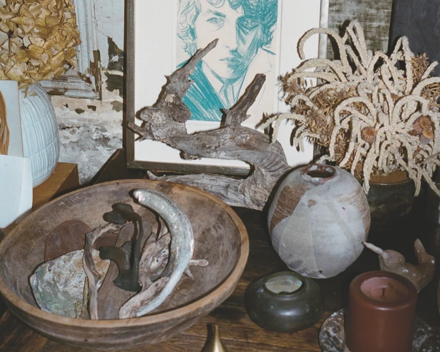 An image from Neptune papers issue 9 of a side table filled with collected decor, a sketch of a man, a ceramic vase, wooden bowl with various objects inside