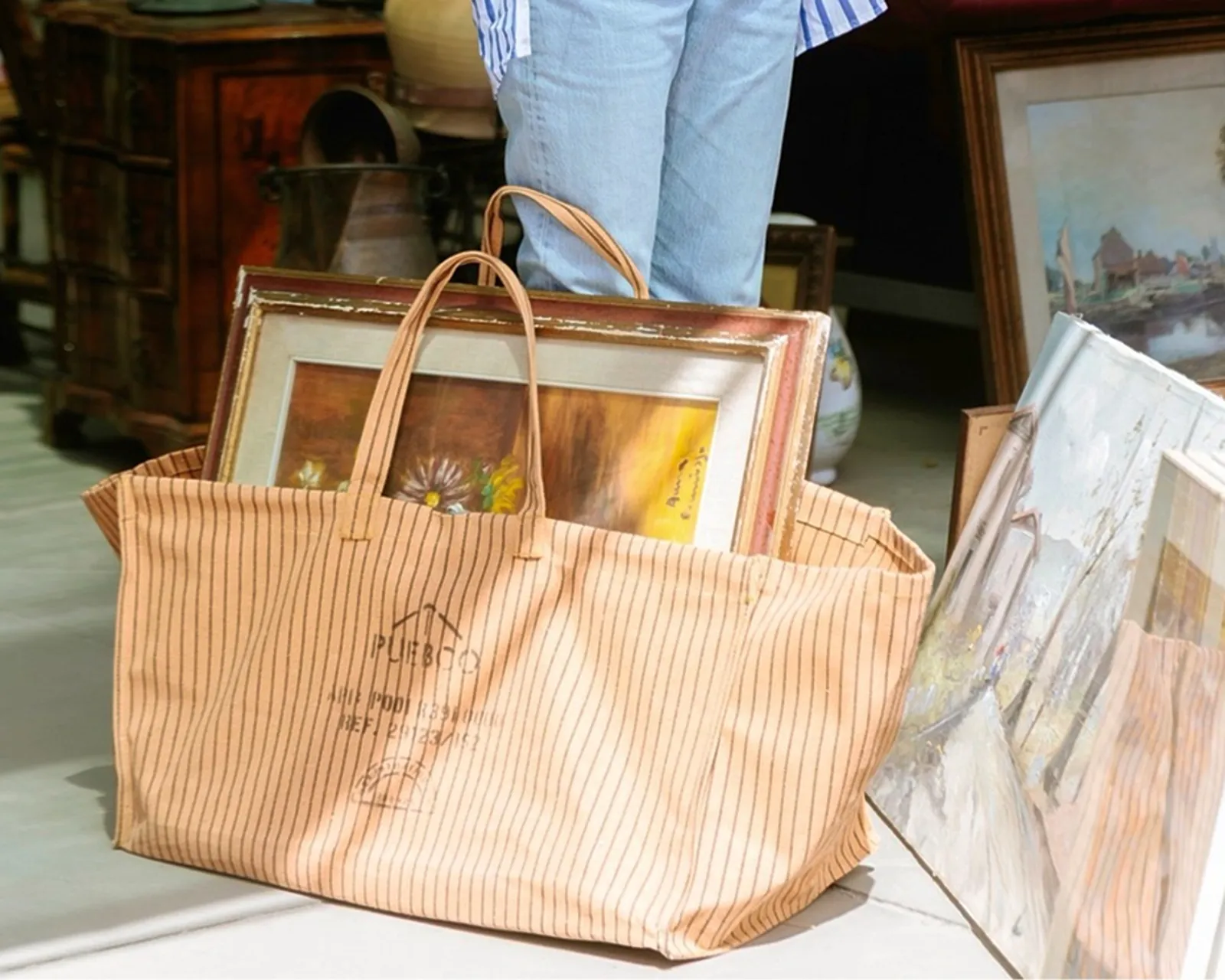 Puebco Waxed Canvas Large Bag in a market setting, carrying framed artwork and vintage finds, crafted from durable waxed cotton with utility-inspired detailing, available at Handcrafted Modern.