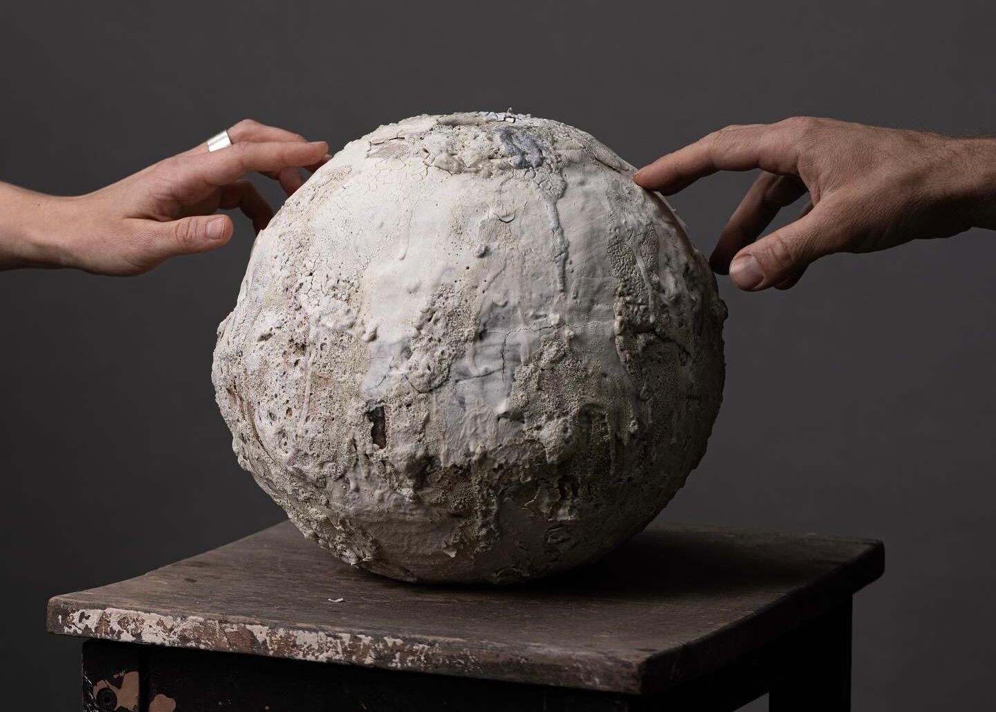 Ceramic sculpture by Maria Loram with heavily textured white clay surfaces, photographed with hands reaching toward the organic spherical form.