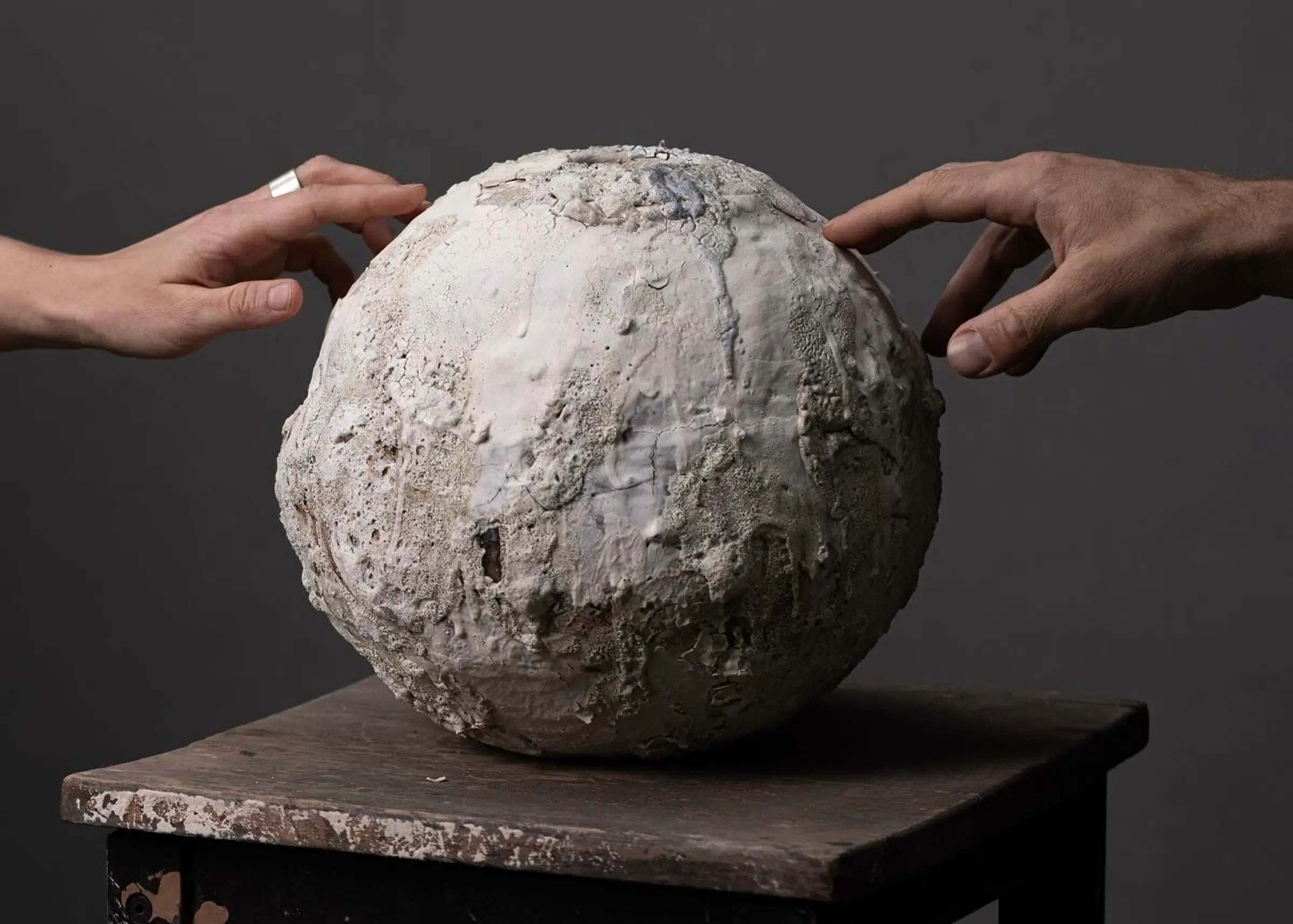 Ceramic sculpture by Maria Loram with heavily textured white clay surfaces, photographed with hands reaching toward the organic spherical form.