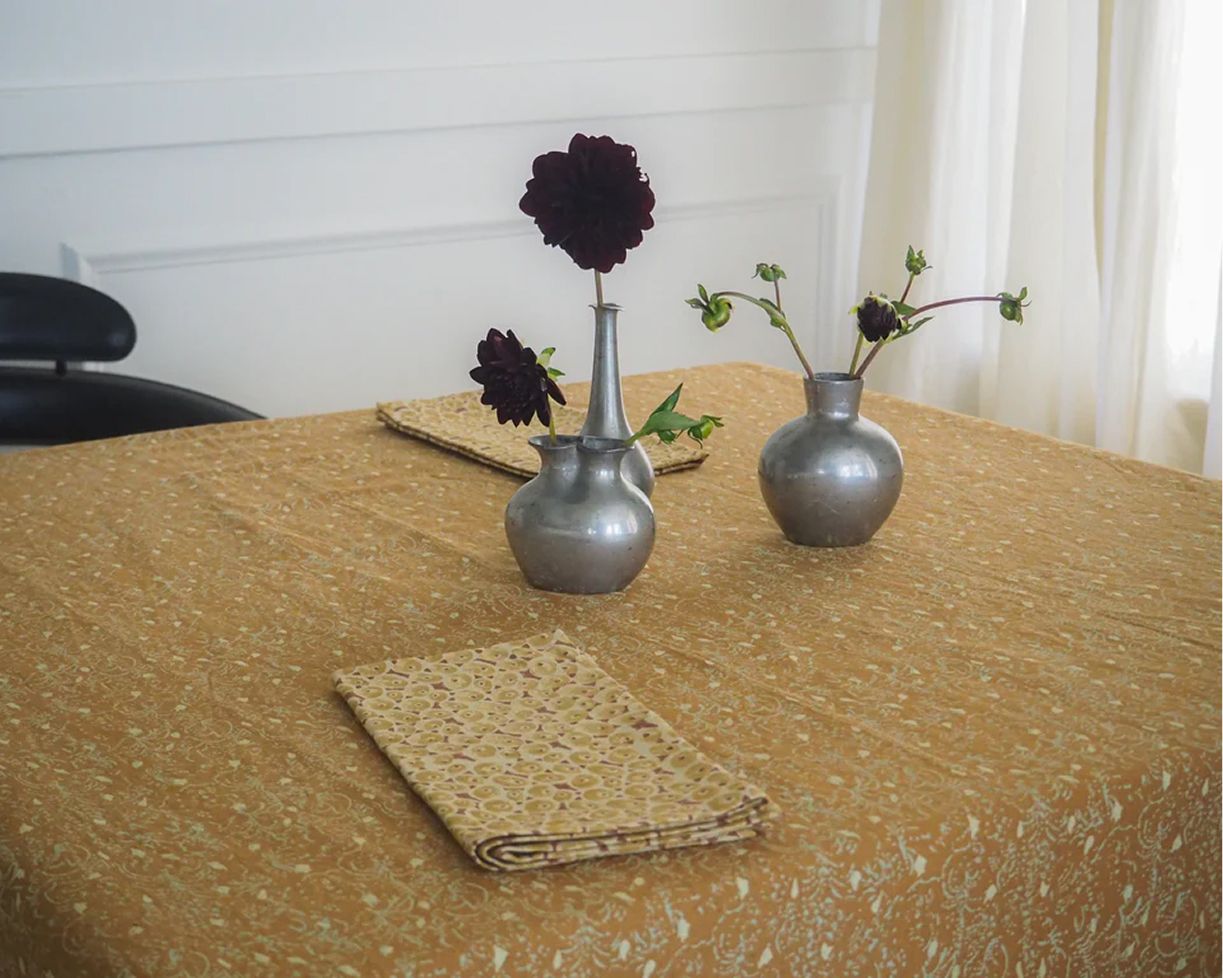Studio Ford Aurea block printed cotton and linen tablecloth in golden ochre, hand-printed textile styled on a dining table with flowers, available at Handcrafted Modern.