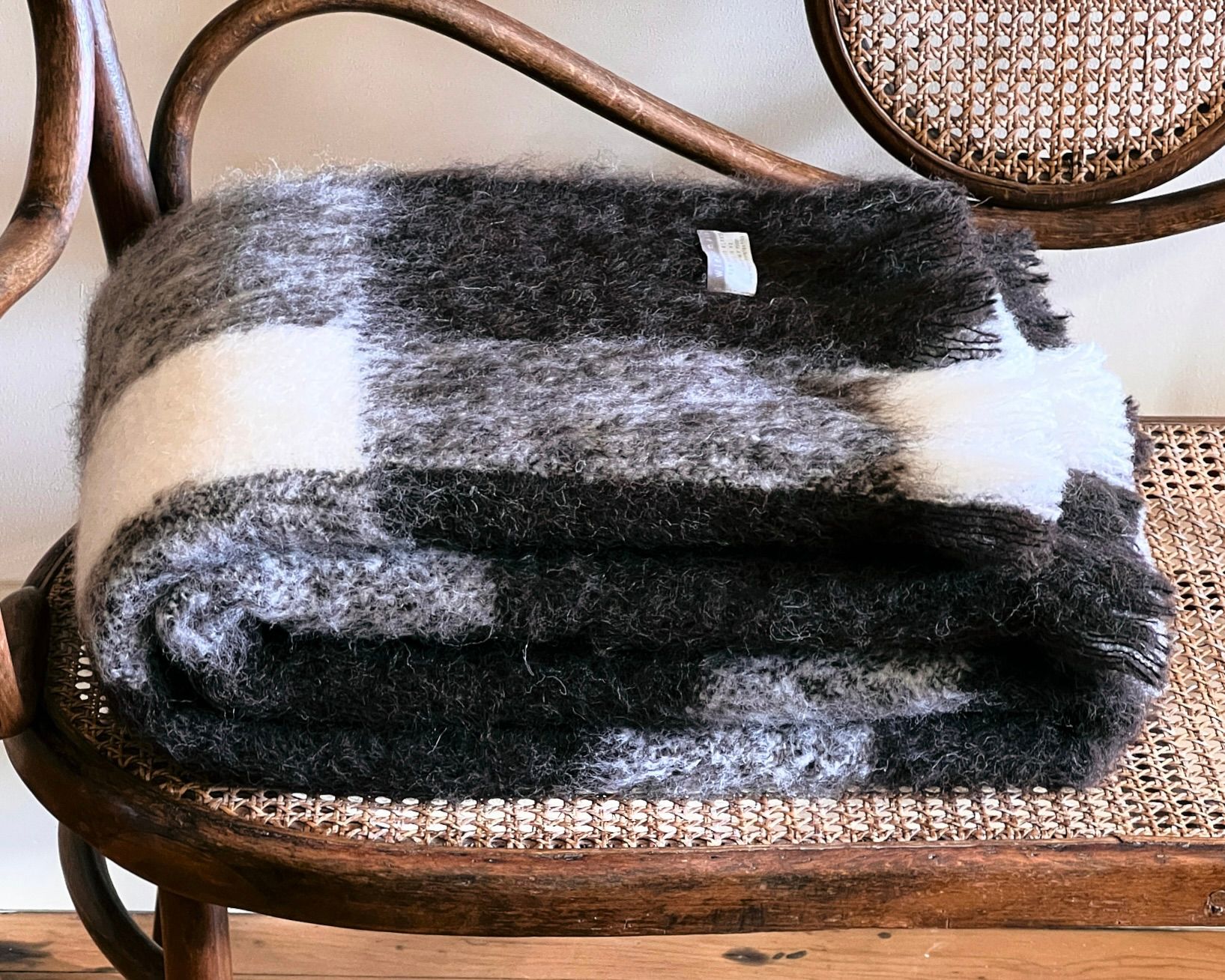 Alpaca wool plaid blanket on a Thonet bentwood bench seat with wicker detail on a cream background