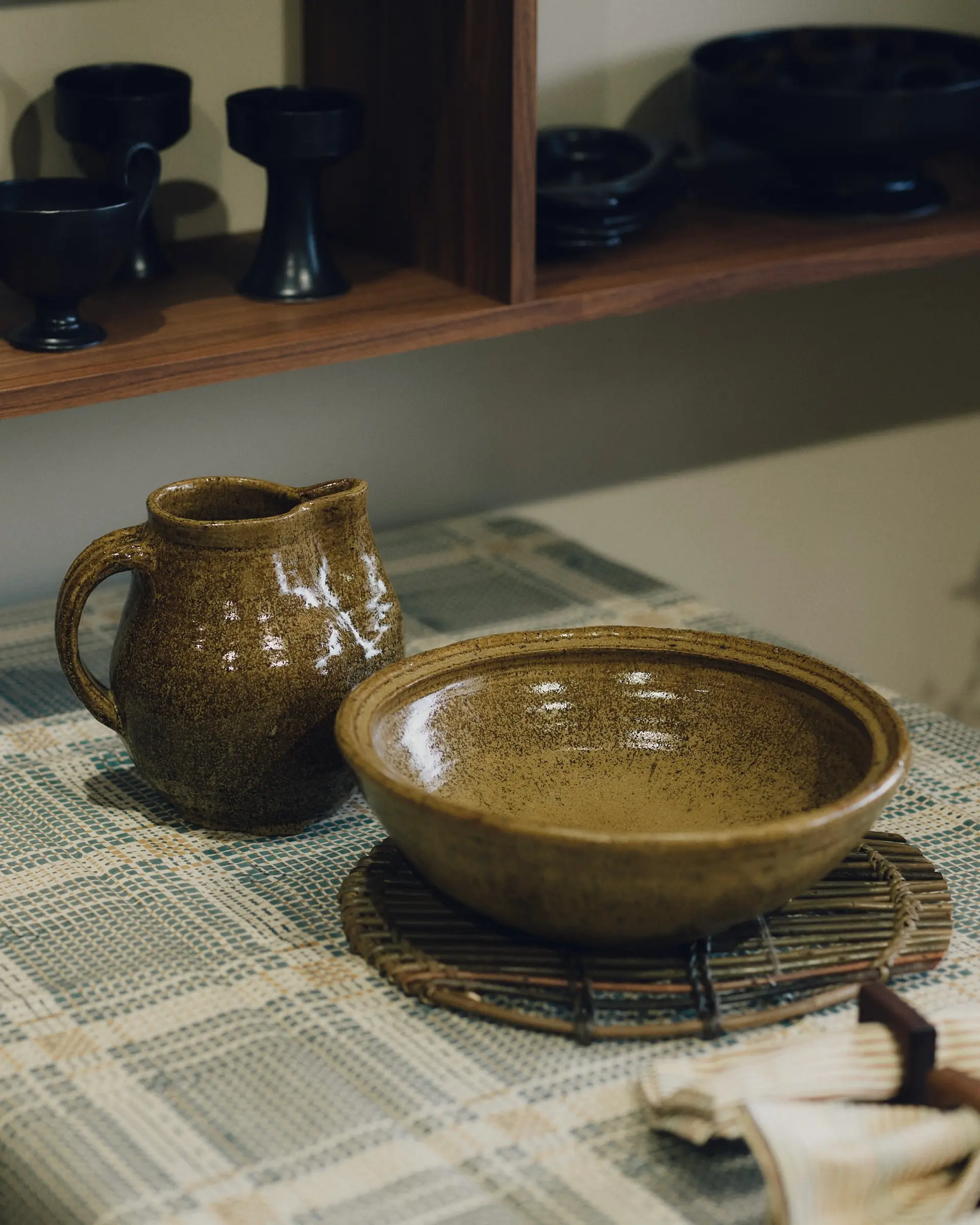 Dryburgh Pottery caramel green glazed harvest jug and large serving bowl on a tabletop with a Studio Ford block-printed tablecloth and woven willow trivet