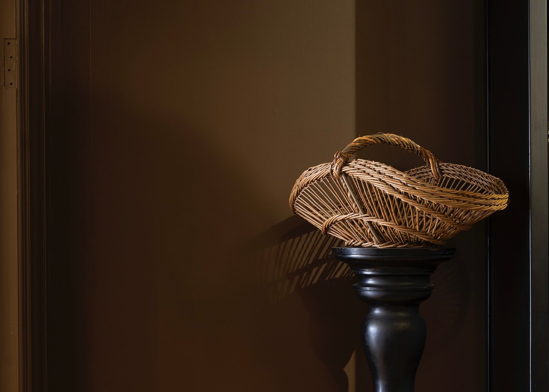 Handwoven Périgord basket by Mike Lilian, woven from natural willow with a traditional curved handle, displayed on a black pedestal in a contemporary interior.