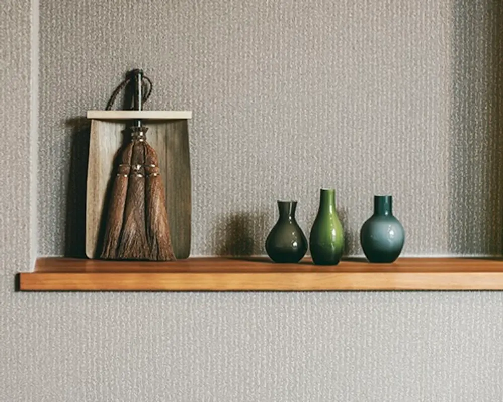 palm fibre broom and wooden dustpan on a shelf next to three glass bud vases
