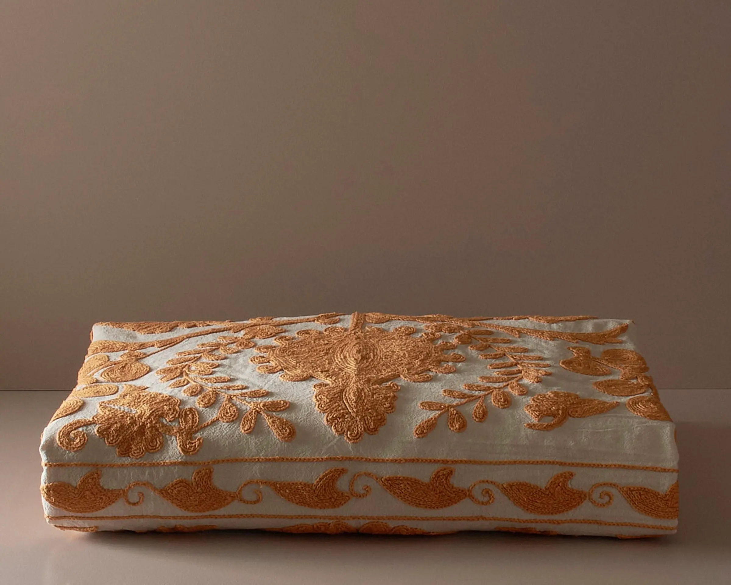 An embroidered suzani bedcover on a neutral colored plinth