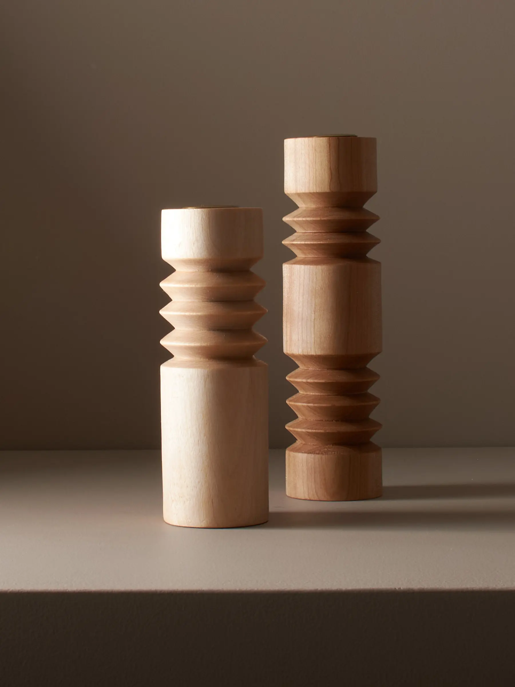 A studio photo of a pair of hand turned wooden ribbed candle sticks on a warm brown background