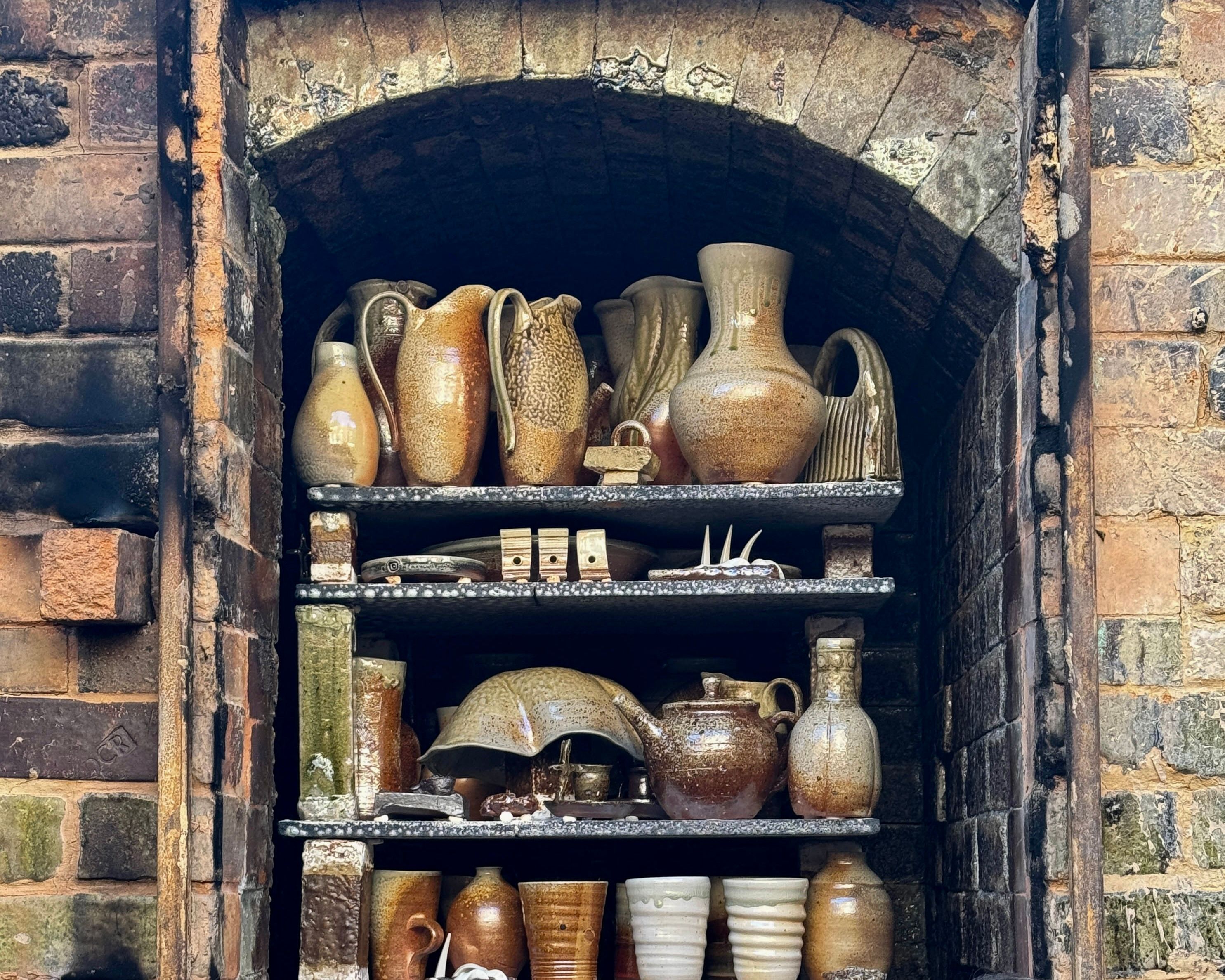 a collection of wood fire ceramics that have just been fired, emerging from the brick kiln. Pieces by ceramic artist Kaiqi qiu with rusty red and sage tones on natural form ceramics vases, jugs and cups