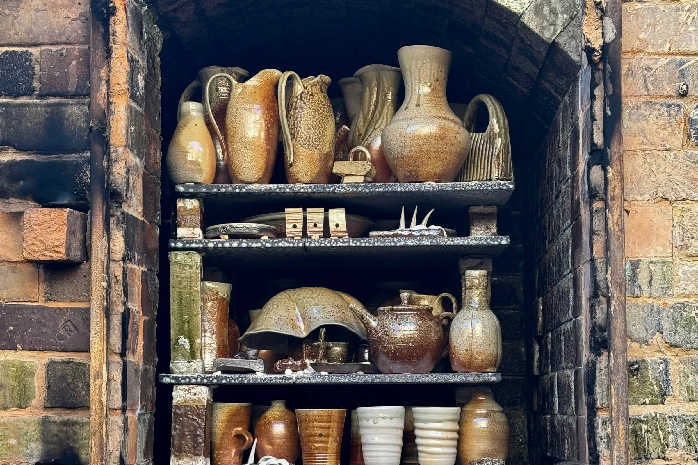 a collection of wood fire ceramics that have just been fired, emerging from the brick kiln. Pieces by ceramic artist Kaiqi qiu with rusty red and sage tones on natural form ceramics vases, jugs and cups